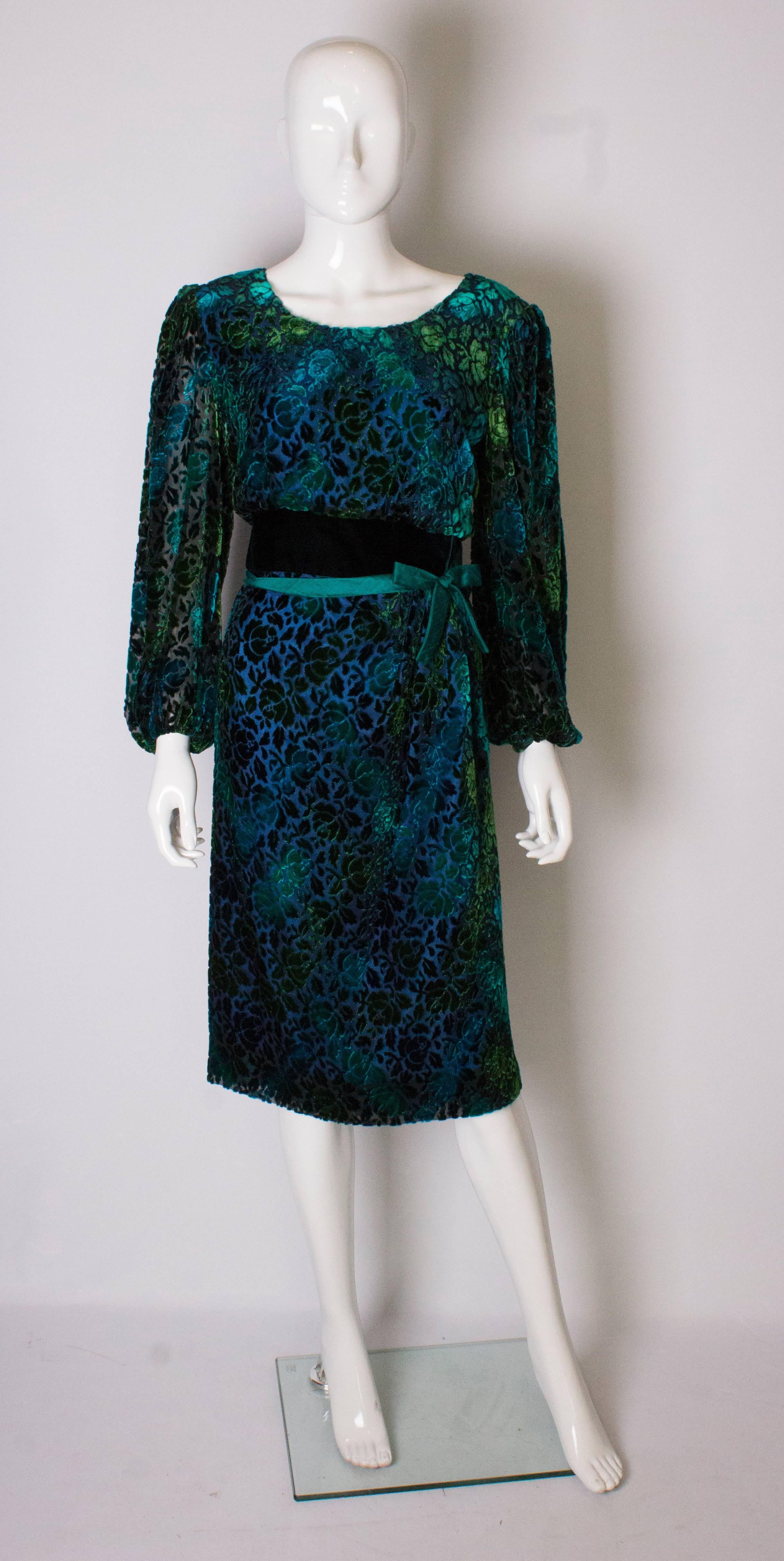 A chic vintage  cocktail dress by Donald Campbell. In wonderful shades of green, the dress has sheer sleeves with elasticated wrists, a scoop neckline, central back zip, is lined in silk and has a velvet waistband.