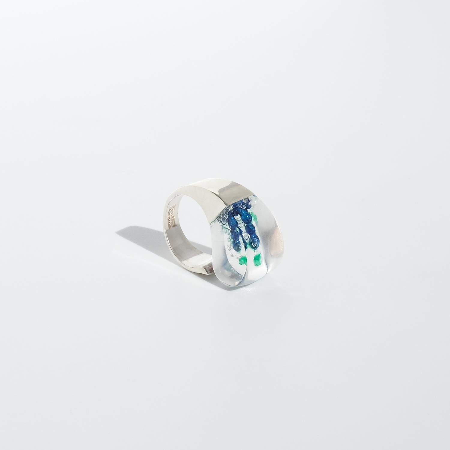 This vintage silver ring features a bold, sculptural design with a wide, fixed band that adds to its striking presence. Its centerpiece is a smooth, domed acrylic element, blending vibrant green and blue hues that create a captivating play of color.