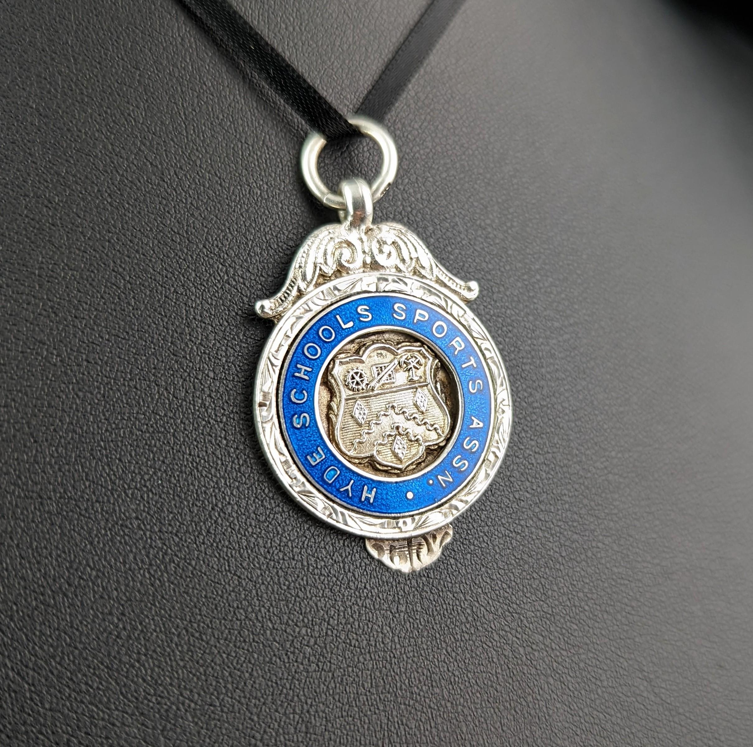 An attractive vintage sterling silver and enamel fob pendant.

It is a circular shaped piece with an attractive vibrant blue enamelled design, the fob has a repousse shield to the centre which is decorated with a number of tiny symbols, a very