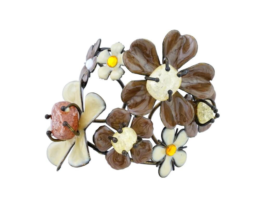 A vintage silver and enamel bangle bracelet with flowers. Alternating flowers of different sizes in brown and cream pearline enamel are attached to the bracelet, almost completely covering the wrist. In the middle of the larger flowers are cores