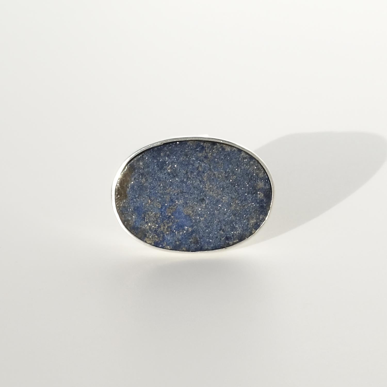 Dieser Vintage-Ring besteht aus einem flachen, ovalen Lapislazuli-Stein, der in Sterlingsilber gefasst ist. Der Stein hat eine tiefblaue Farbe mit subtilen Flecken von Goldpyrit, die ihm einen natürlichen Schimmer verleihen. Die Fassung der Lünette