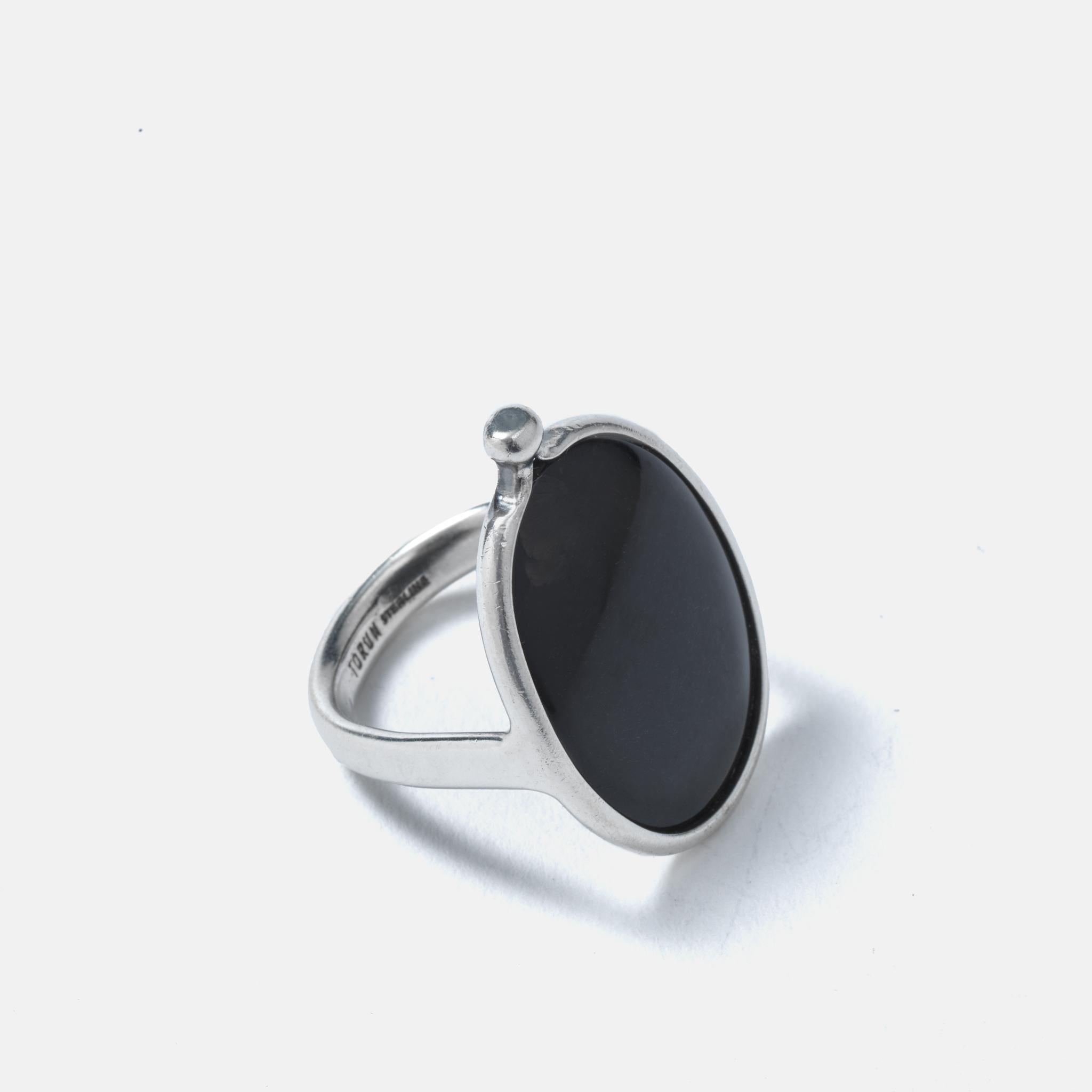 This sterling silver ring is adorned with an oval shaped mother of pearl stone. On one side the framing ends up in a bundle which gives the ring an intriguing look. The mother of pearl stone has a matte black colour and with that something that