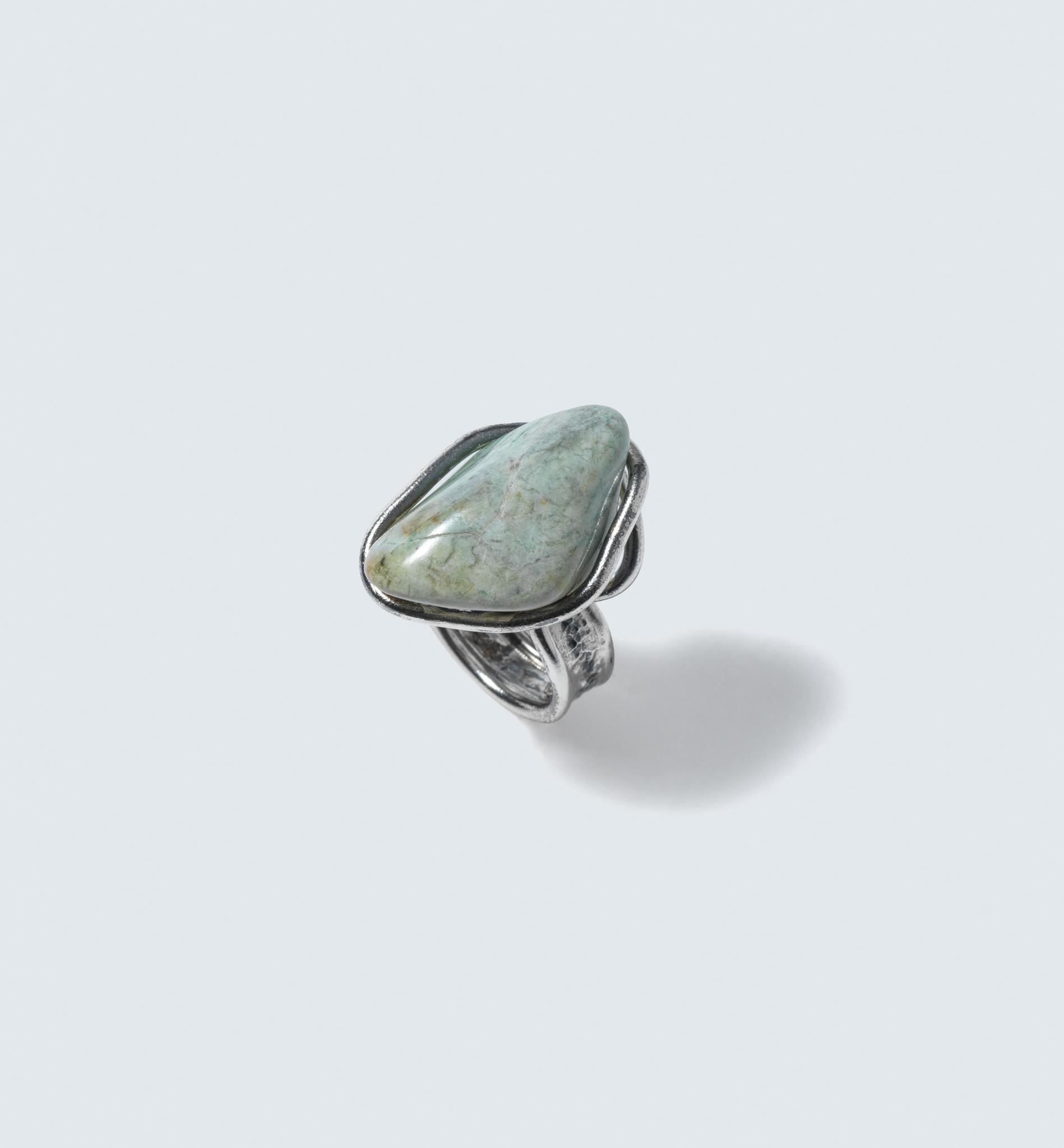 This is a unique ring that features a large, mint green natural stone set atop a silver band. The stone is secured with an unconventional setting, where a silver wire is wrapped around it, creating a distinctive and artistic look. The band of the