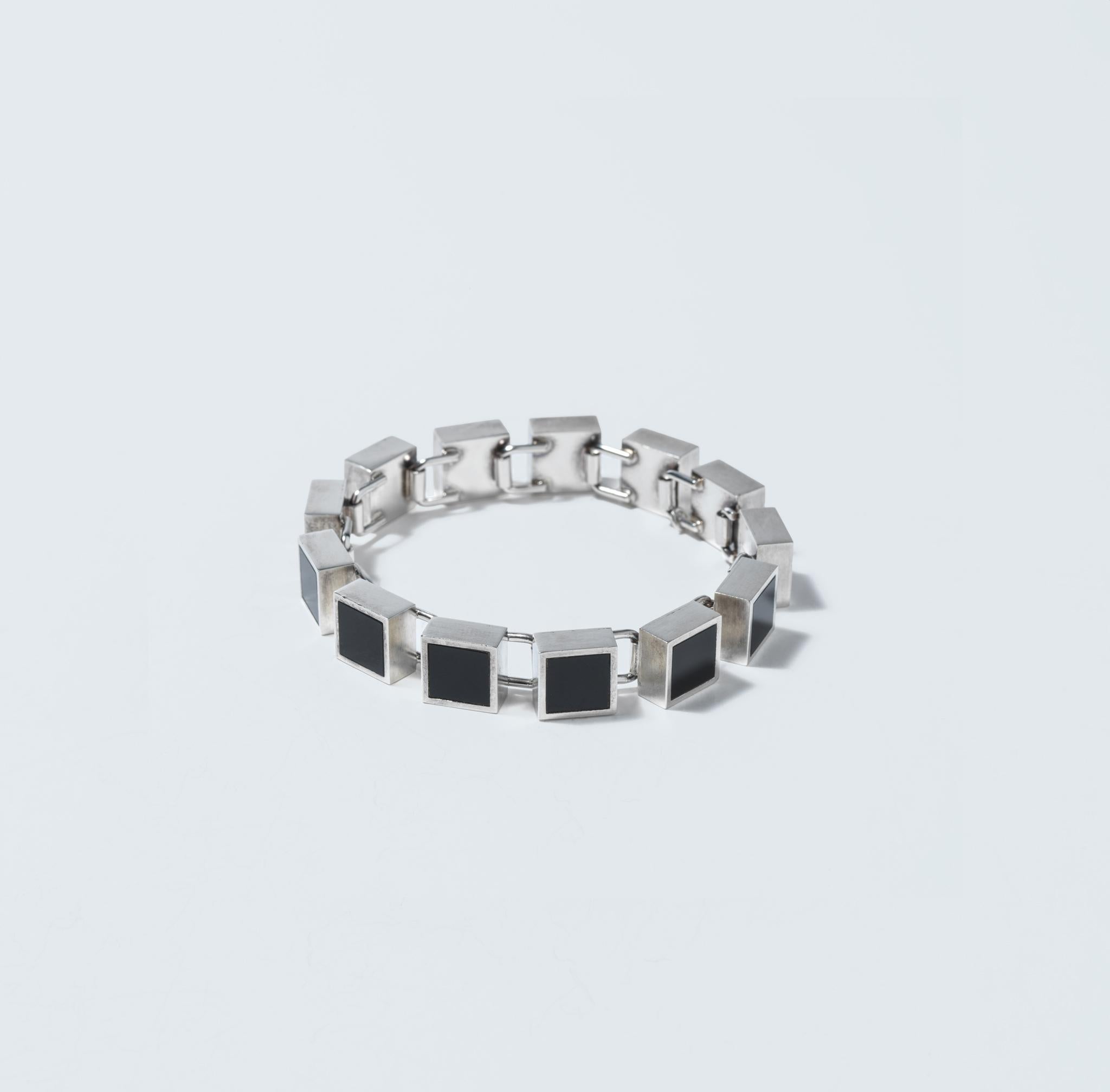 Ein zeitloses Stück Eleganz, ein Armband aus Sterlingsilber aus den 1970er Jahren, entworfen von dem bekannten Schmuckdesigner Arne Johansen.

Dieses exquisite Armband zeigt quadratische Onyxsteine, die sorgfältig in silberne Fassungen gefasst sind