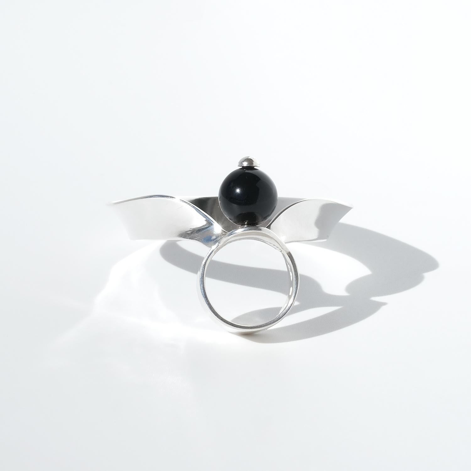 Questo anello d'argento vintage presenta un'impressionante pietra onice rotonda, coronata da un pomello d'argento lucido al centro. Il design va oltre la tradizionale forma dell'anello con un ornamento in argento che si estende elegantemente sul