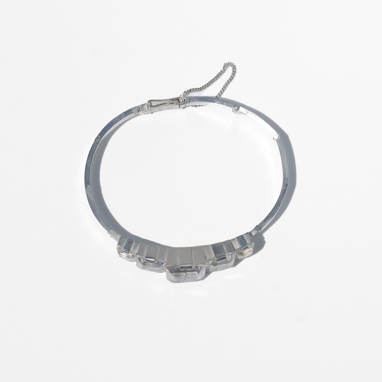 This vintage silver bracelet features five clear rock crystal stones arranged in a graduated sequence, with the largest stone set in the center. The emerald-cut crystals are mounted in bold, geometric Art Deco-style settings. The silver band is