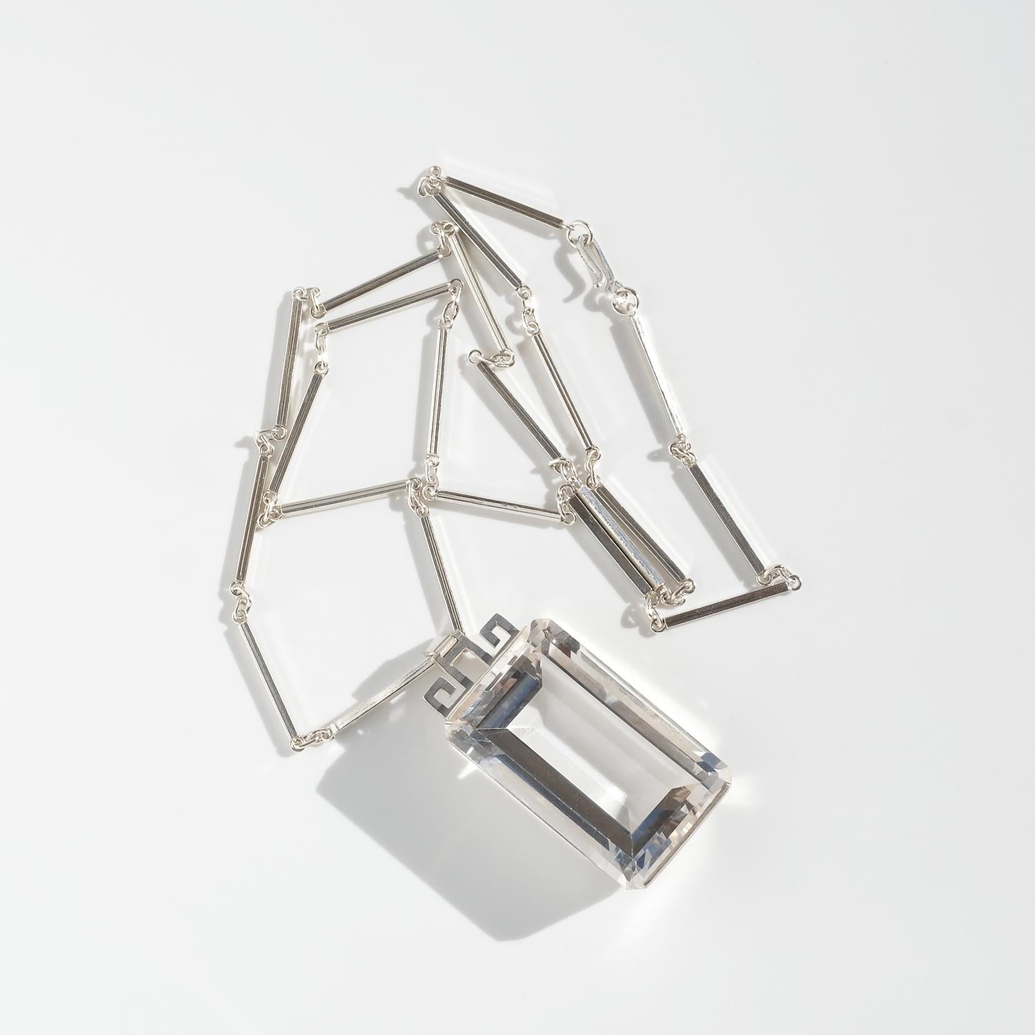 Questa straordinaria collana è realizzata in argento con un ciondolo con un grande cristallo di rocca rettangolare sfaccettato. Il ciondolo è sostanzioso, con linee pulite e geometriche e una robusta cornice d'argento che trattiene saldamente la