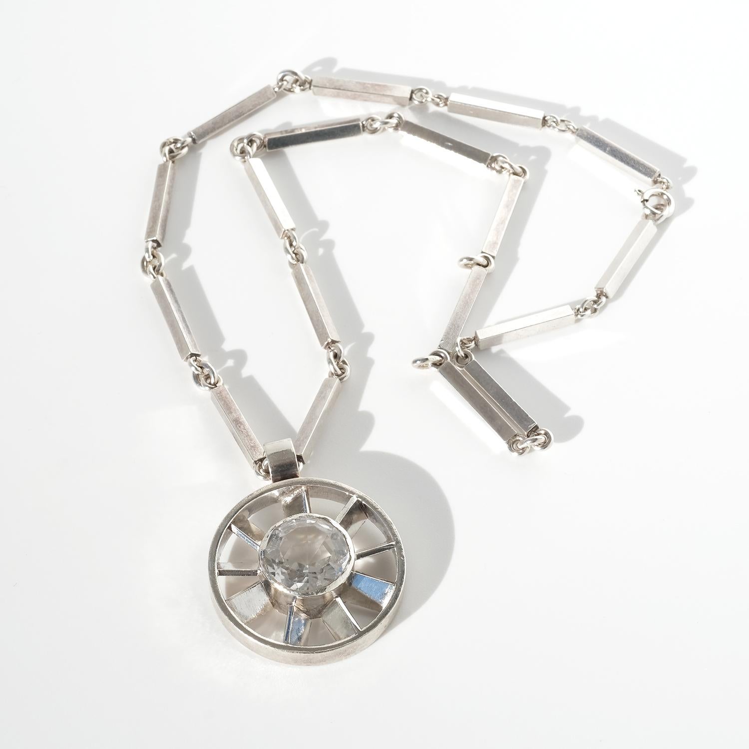 Questa collana d'argento vintage presenta un audace ciondolo circolare che ricorda una ruota, con al centro un cristallo di rocca sfaccettato che brilla in modo brillante. La sostanziosa catena, composta da barre d'argento allungate collegate da