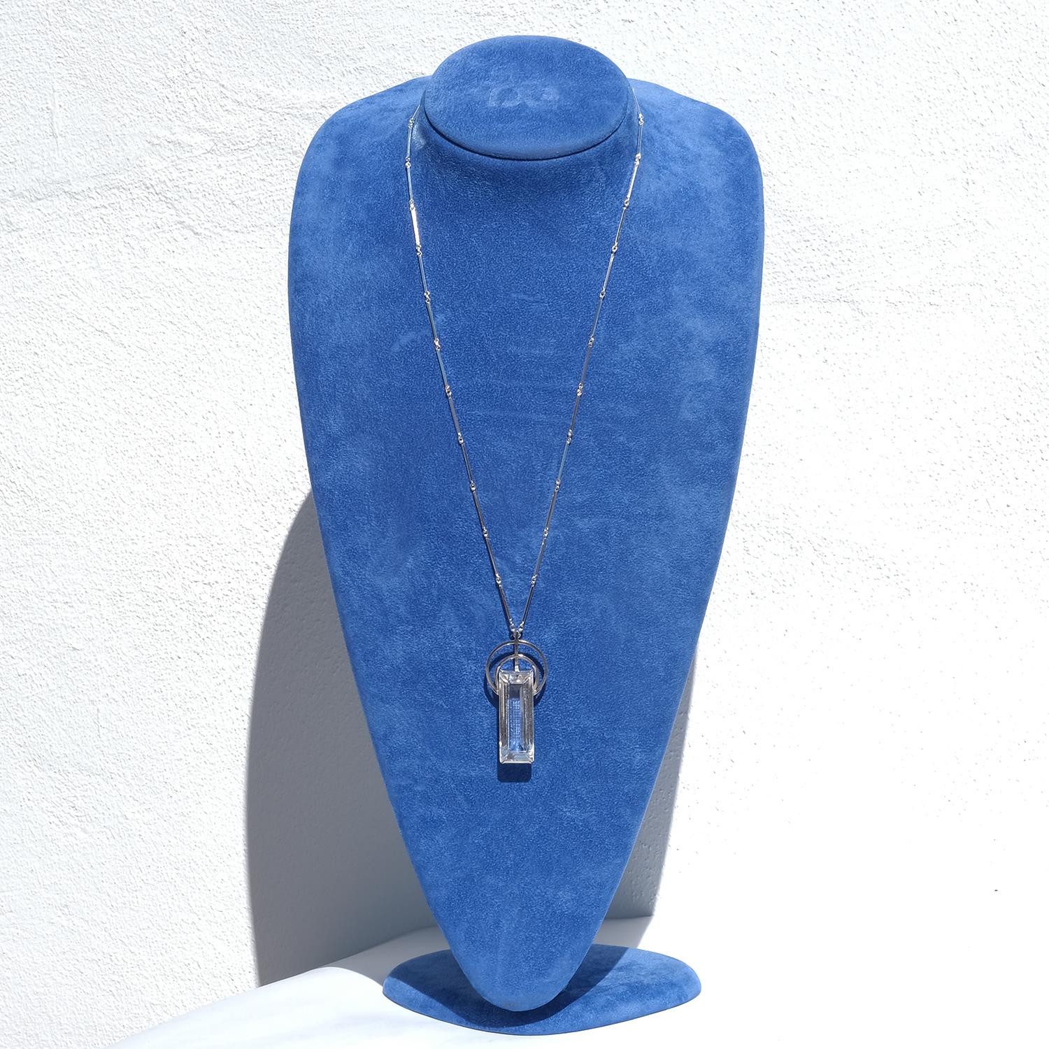 This vintage necklace features a classic silver bar-and-ring chain with a symmetrical layout. At the center hangs a striking rectangular pendant set with a clear, faceted rock crystal, cut in an elongated shape. Two concentric silver circles sit