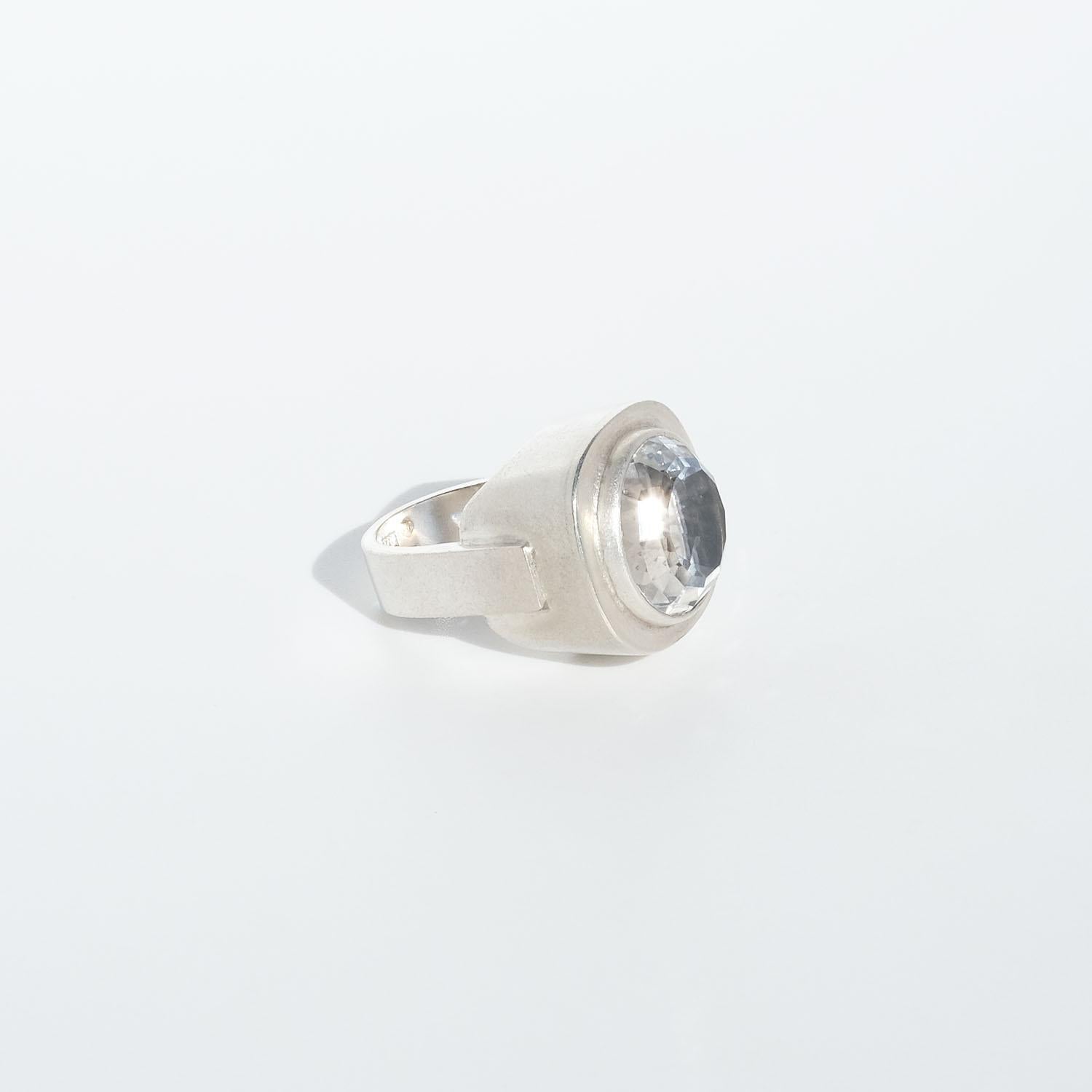 This powerful sterling silver ring is adorned with a faceted rock crystal. The setting is shaped like a silver bowl from which the rock crystal arises. The shank is u-shaped and attached on the setting’s outer sides.

The ring has a roman style to