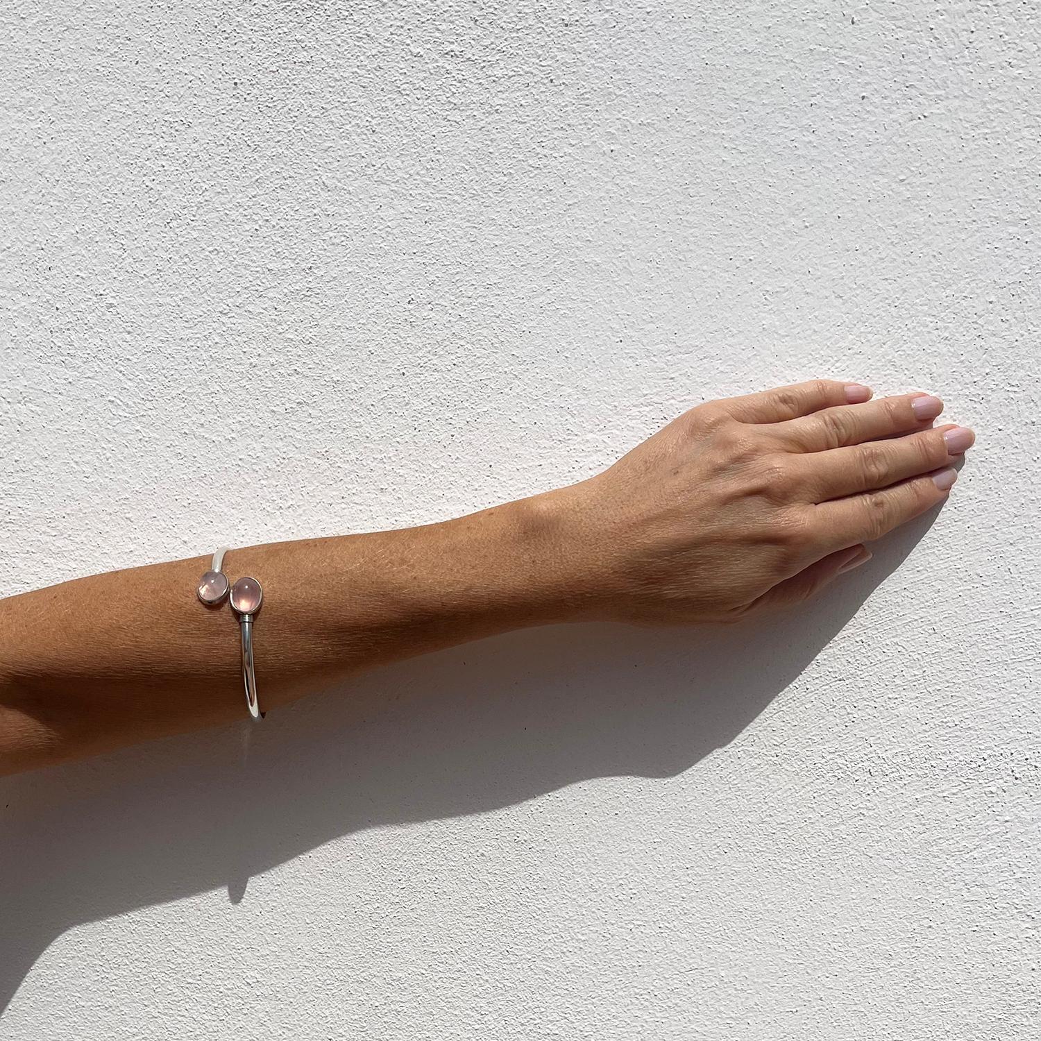Ce bracelet manchette en argent sterling est orné de deux belles pierres de quartz rosé taillées en cabochon. Le bracelet manchette descend doucement le long du poignet, mais il peut tout aussi bien être porté vers le haut du bras, car il est