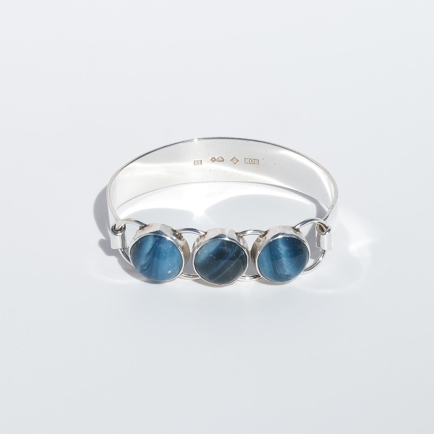 This vintage bracelet is crafted in silver and features a gently tapering band that narrows toward the top, where three round cabochon-cut Swedish Blue pieces (Sw. Bergslagensten) form the central focus. The stones, with their deep, shifting blue