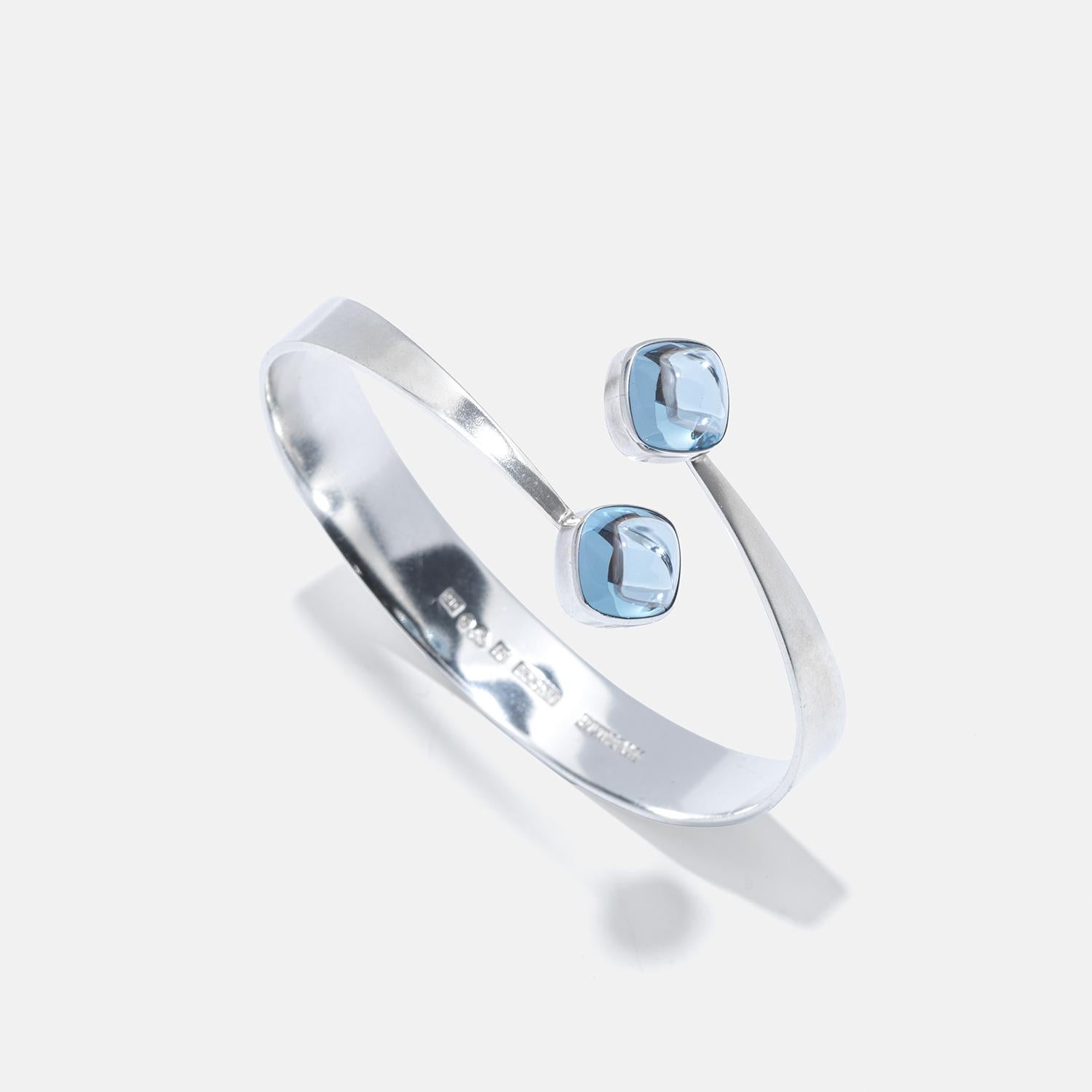 Questo raffinato bracciale in argento presenta spinelli cabochon di colore azzurro incastonati in eleganti cornici quadrate. La fascia, disegnata ad arte per essere più larga nella parte inferiore e assottigliarsi con grazia verso le gemme, emana