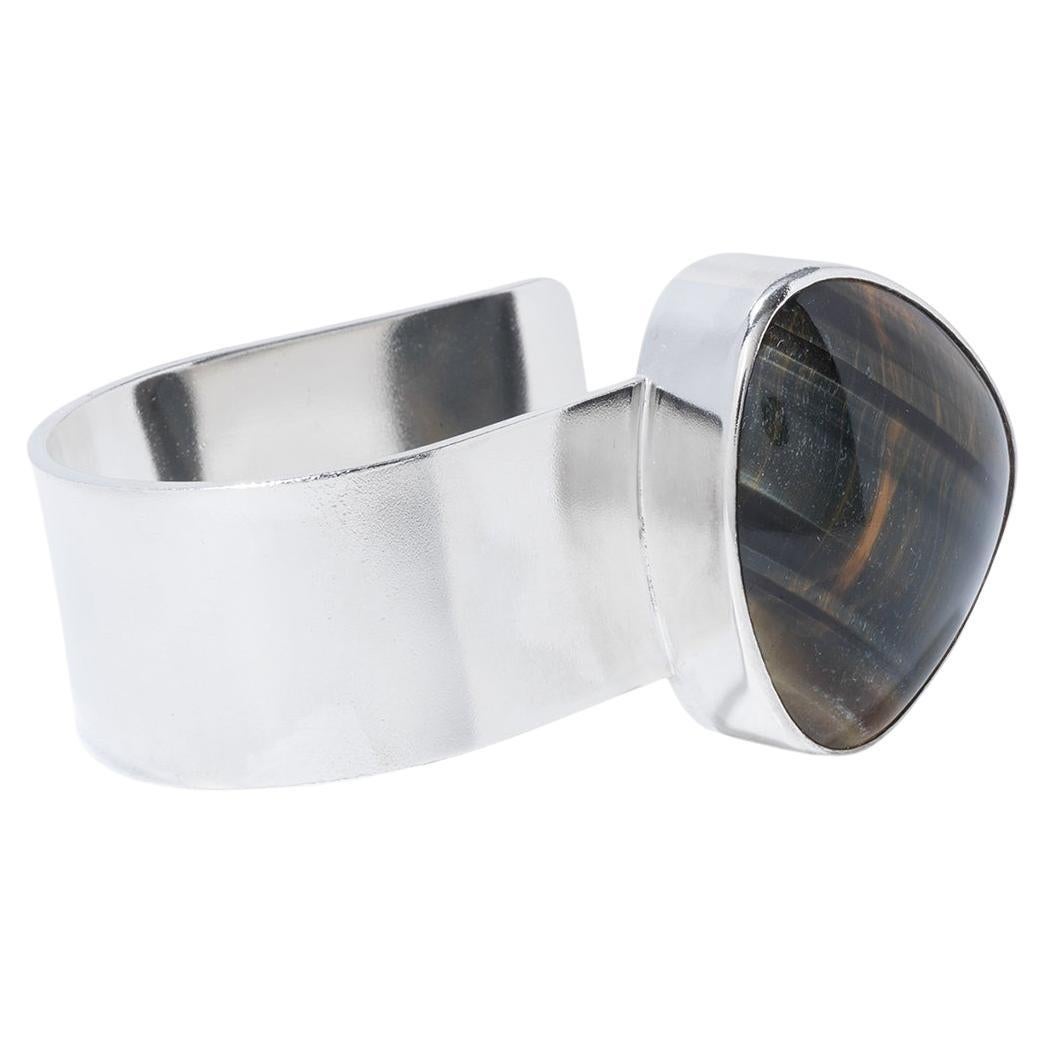 This exquisite bracelet is masterfully crafted from sterling silver and features a prominent, triangle shaped tiger's eye gemstone. The gemstone is set on a wide, elegantly designed silver band, which showcases the tiger's eye's dynamic shift from