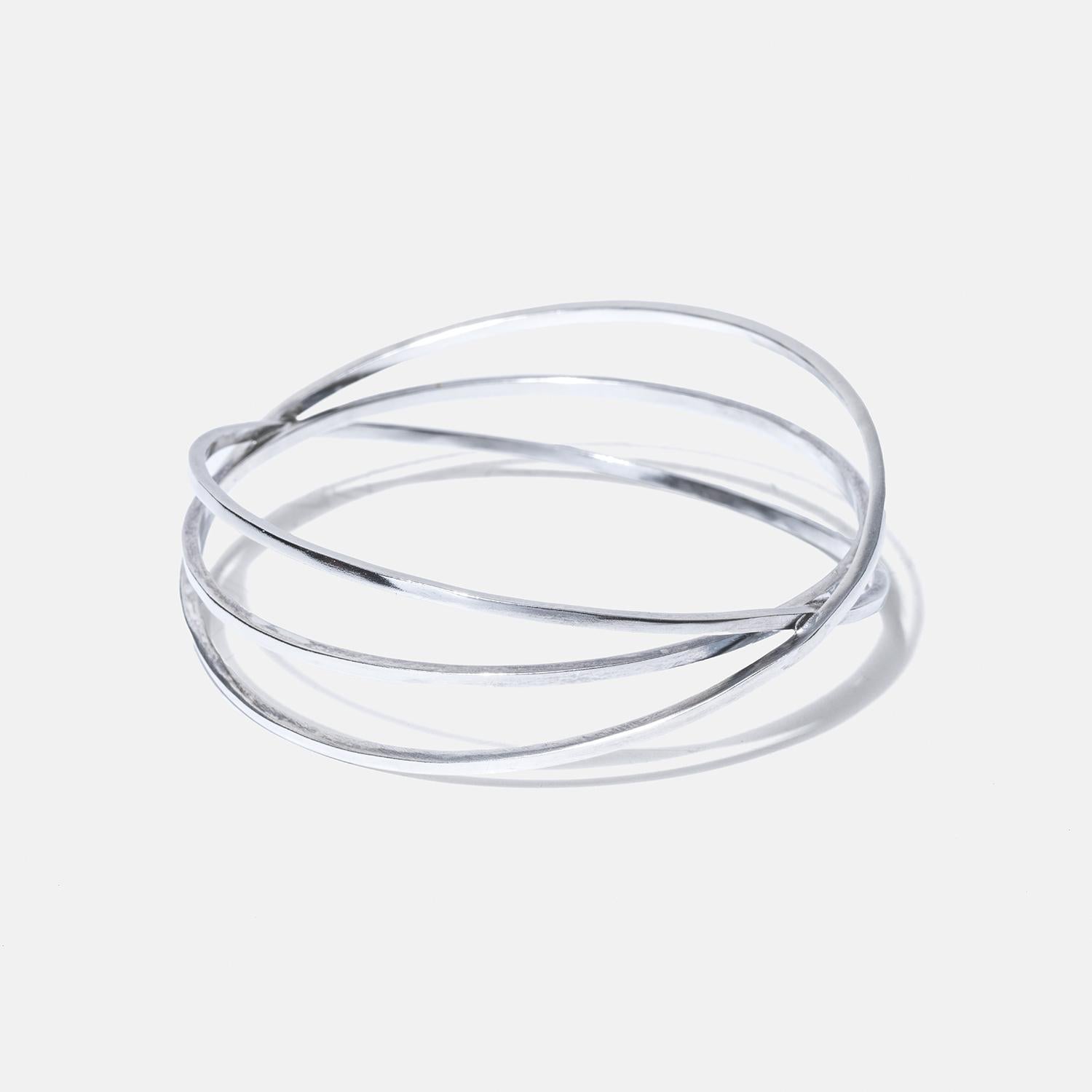 This sterling silver cuff bracelet elegantly consists of three interconnected slim circular bands, creating a harmonious, layered look. Each band is polished to a high shine, reflecting light beautifully and emphasizing its sleek, modern design. The