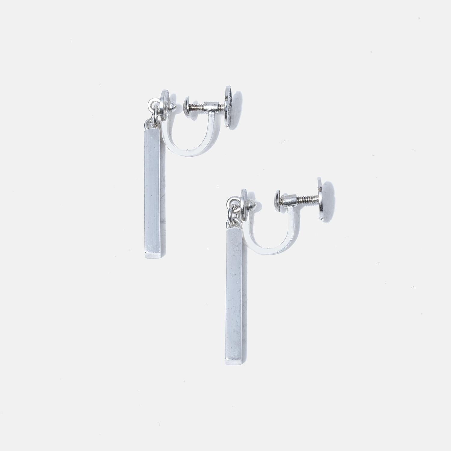These classic silver bar earrings exude understated elegance with their sleek, straight form. They dangle gracefully from the ear, providing a subtle movement that catches the light. Their design is timeless, offering versatility that complements