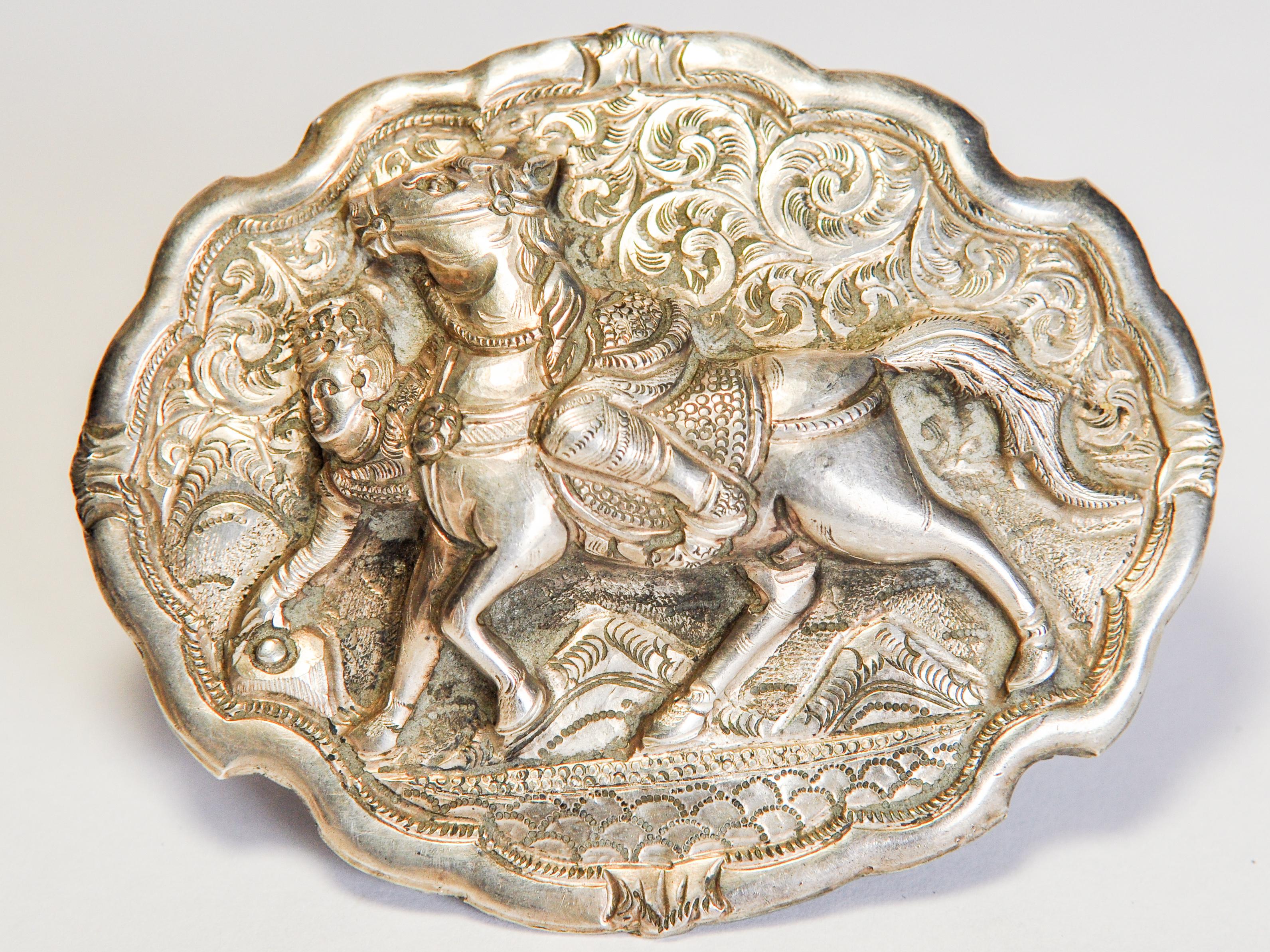 Vintage silver belt buckle with horse & rider motif. From Burma. Mid-20th century. Repousse work and chasing.
This finely worked buckle features an animated scene of horse and rider in the heat of an equestrian competition. 
Condition: It is in