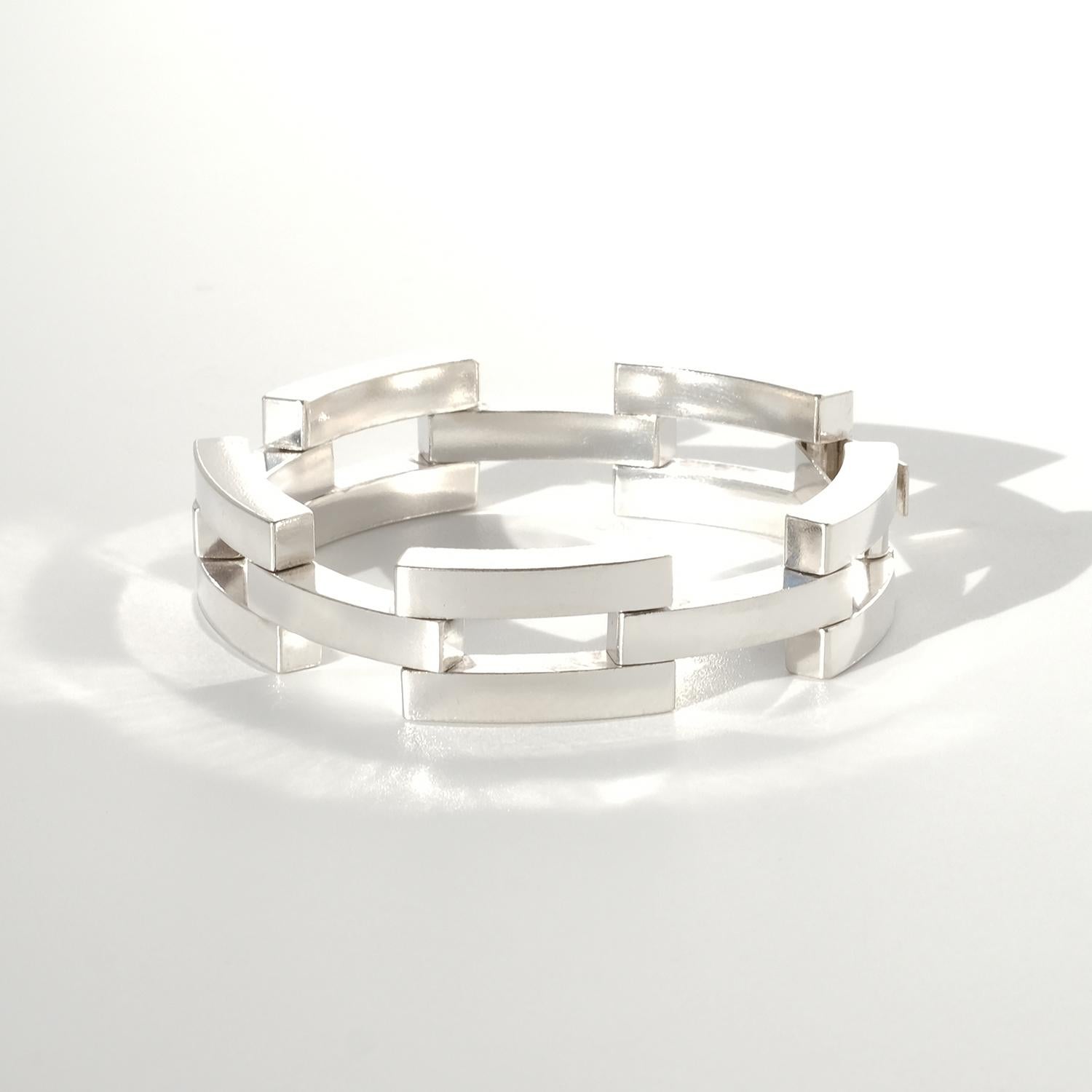 This vintage silver bracelet features a series of interlocking rectangular links, each designed with cut-out rectangular sections that create a sense of depth and structure. The surface has a slightly aged, matte finish, enhancing its bold,