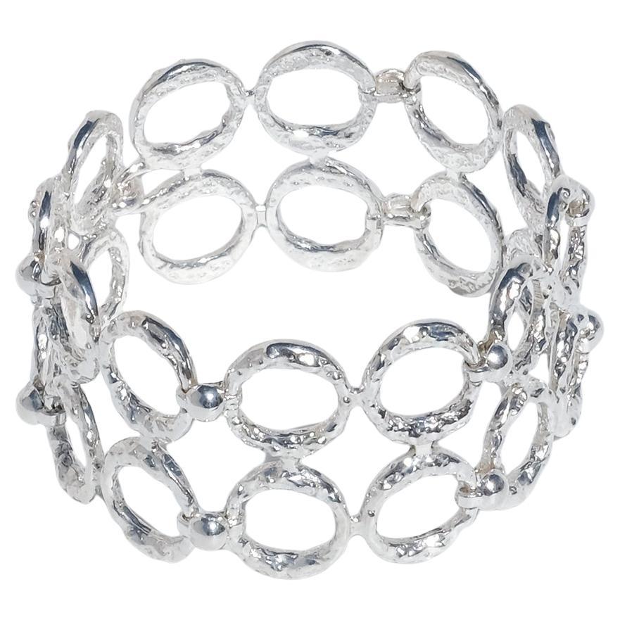 This bracelet is crafted from sterling silver and built from rows of hammered circular elements arranged in two parallel lines. Each ring has a richly textured surface that catches and scatters light. The open circles are connected by discreet