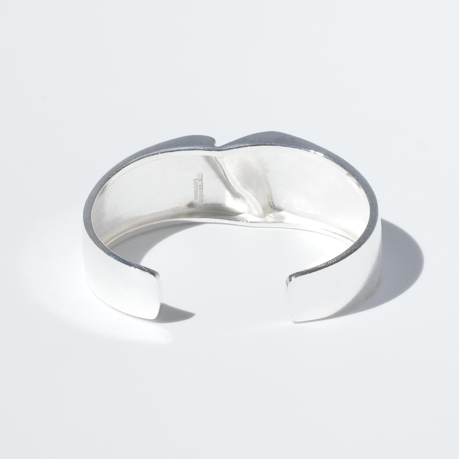 This vintage silver cuff bracelet, known as Darina’s Bracelet, has a bold yet refined design. The surface combines a bright and brushed finish, creating a subtle contrast that enhances its sculptural quality. At the center, a recessed, folded detail