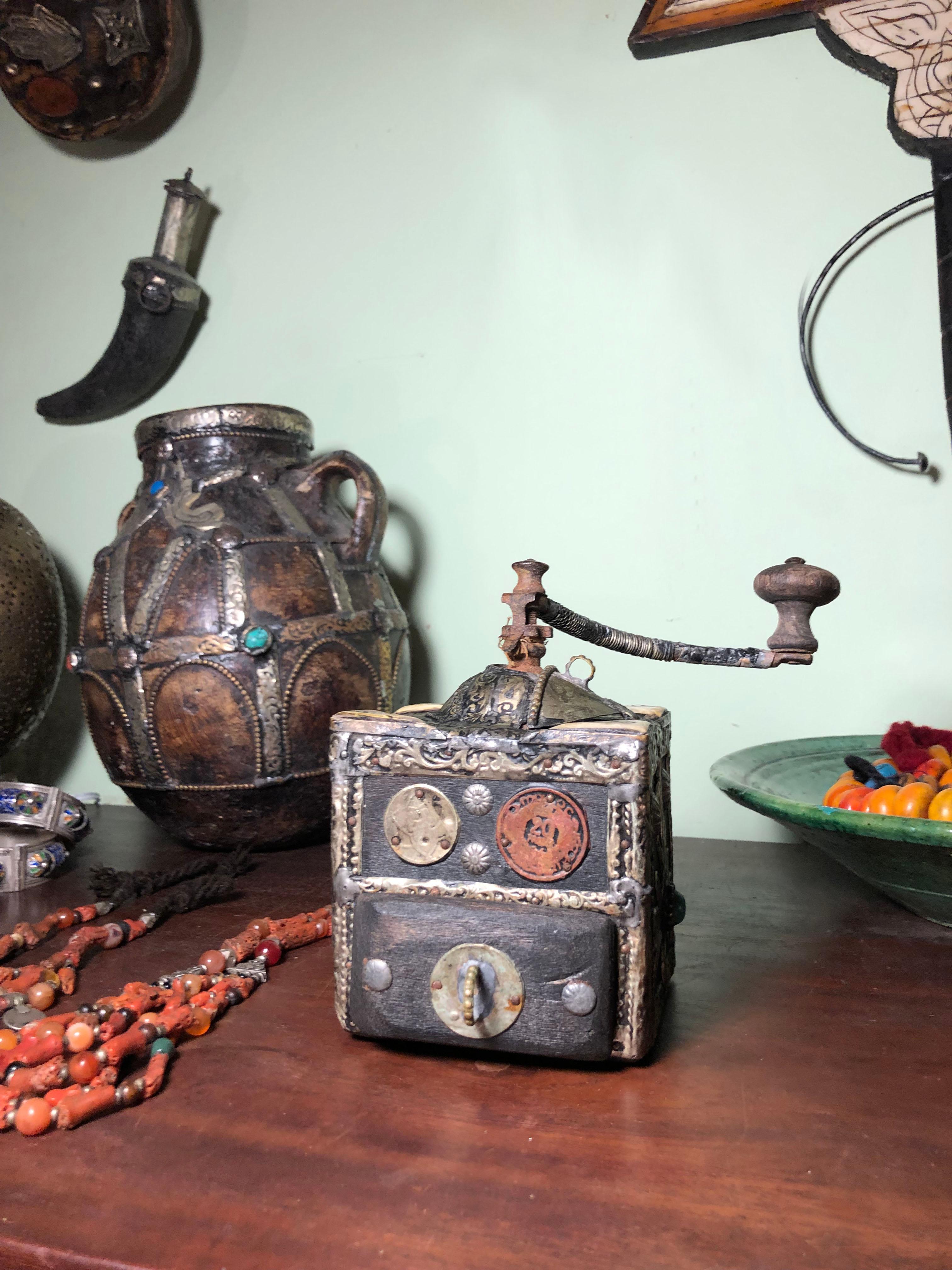 This antique coffee grinder is made of ebony wood, with hand-engraved silver melange adornment, hand-carved camel bone embellishments, and two coins. Entirely handmade, this grinder was used by southern Morocco nomads while traveling and crossing
