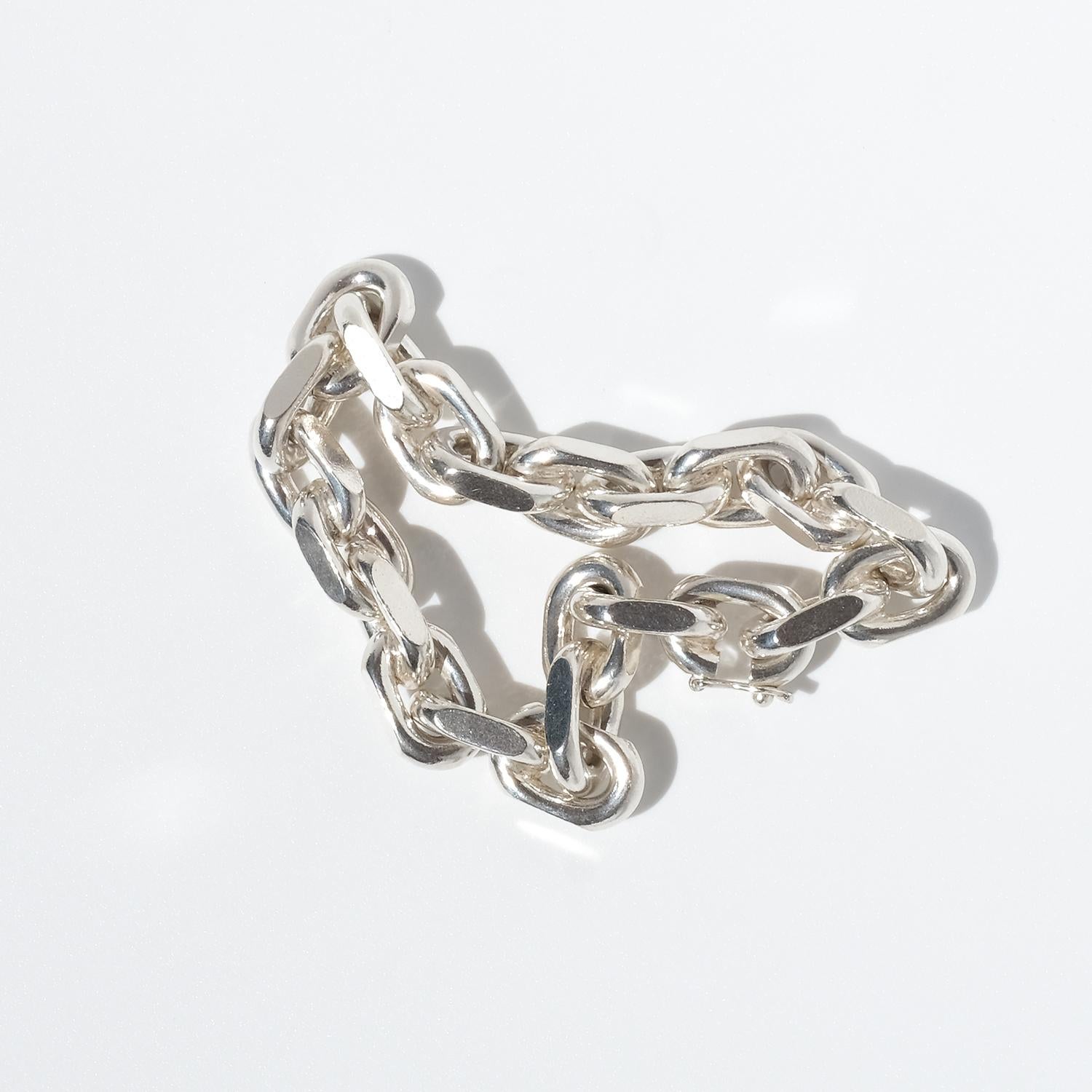 Ce bracelet en chaîne en argent vintage est composé de maillons massifs de forme ovale, chacun présentant une combinaison unique de bords extérieurs arrondis et de panneaux latéraux plats. Les maillons sont assemblés dans une structure continue et