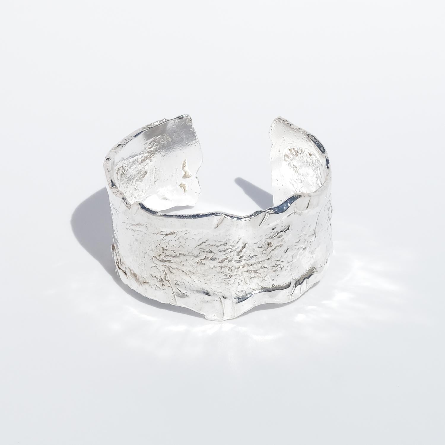 This vintage cuff bracelet is crafted in silver and features an organically contoured form with uneven, sculpted edges that give it a raw, expressive character. The band is relatively wide and has a richly textured surface with deep hammering and