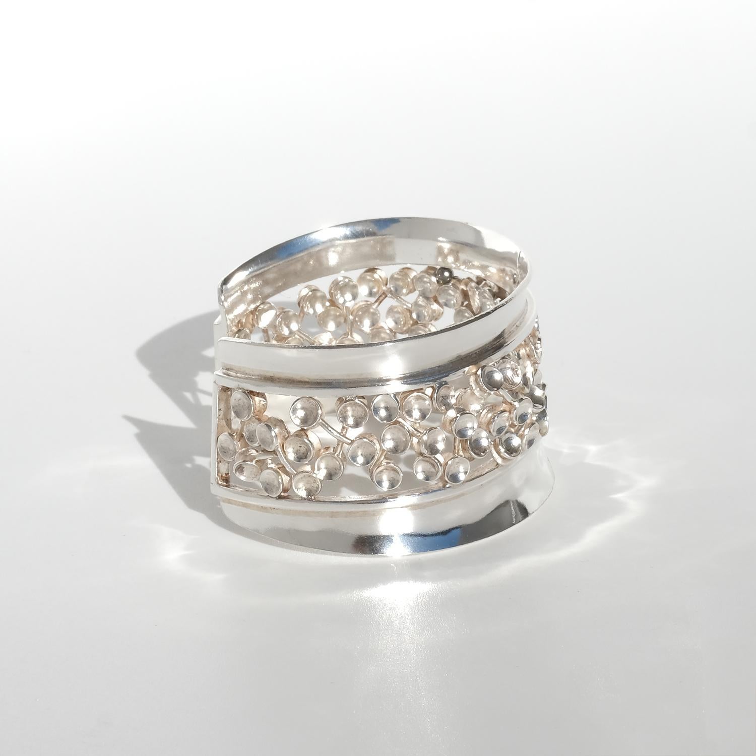 This vintage silver cuff bracelet features a wide, bold design with a central openwork pattern resembling clusters of delicate silver berries connected by fine stems. The intricate detailing contrasts beautifully with the smooth, polished edges,