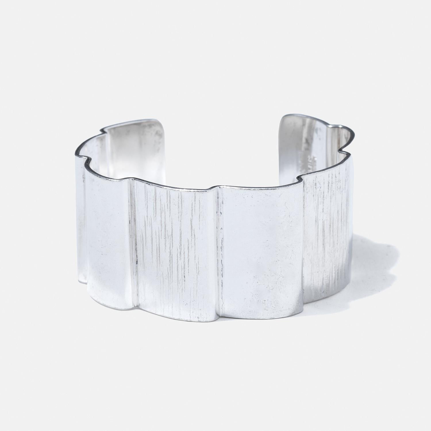 Ce bracelet manchette en argent sterling présente un design ondulé unique qui ajoute un élément visuel dynamique à sa structure. Elle présente une largeur importante, ce qui lui confère une présence audacieuse et proéminente au poignet. La surface