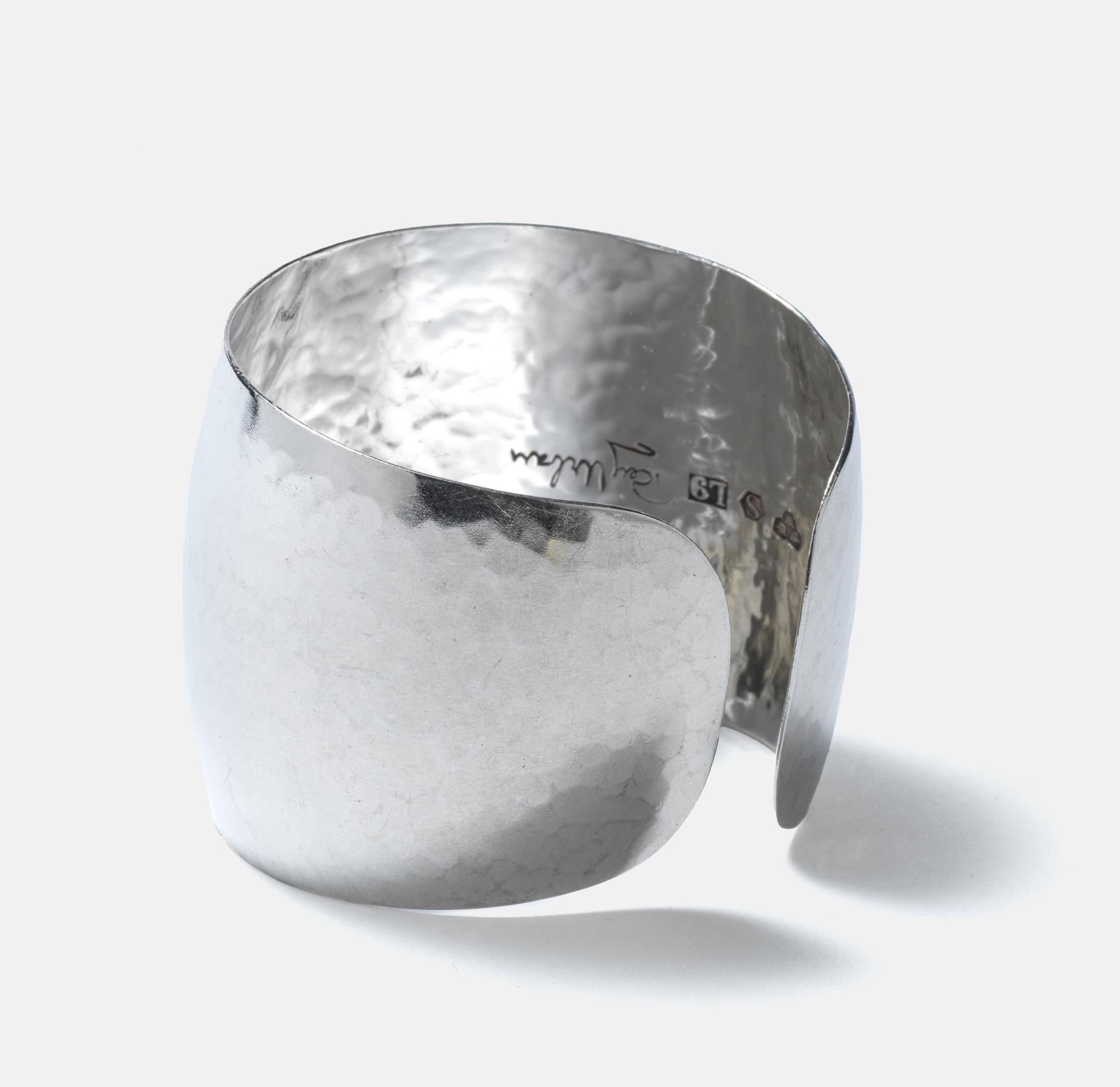 This sterling silver cuff bracelet has a glossy and hammered surface, and also a beautiful arched shape. It may be described as strong, simple and on point. 
This is an early work by Rey Urban and as always the early works are the best.

The