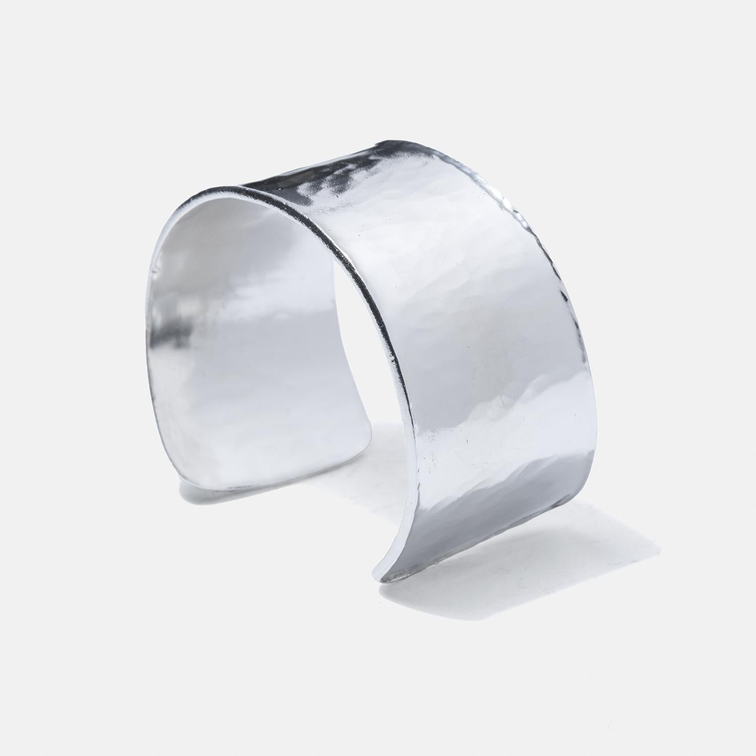 This sterling silver cuff bracelet features a broad, slightly curved band with deliberately uneven, slightly tapered ends, enhancing its artisanal charm. Its surface displays a textured, hammered finish that catches light and adds a rugged yet
