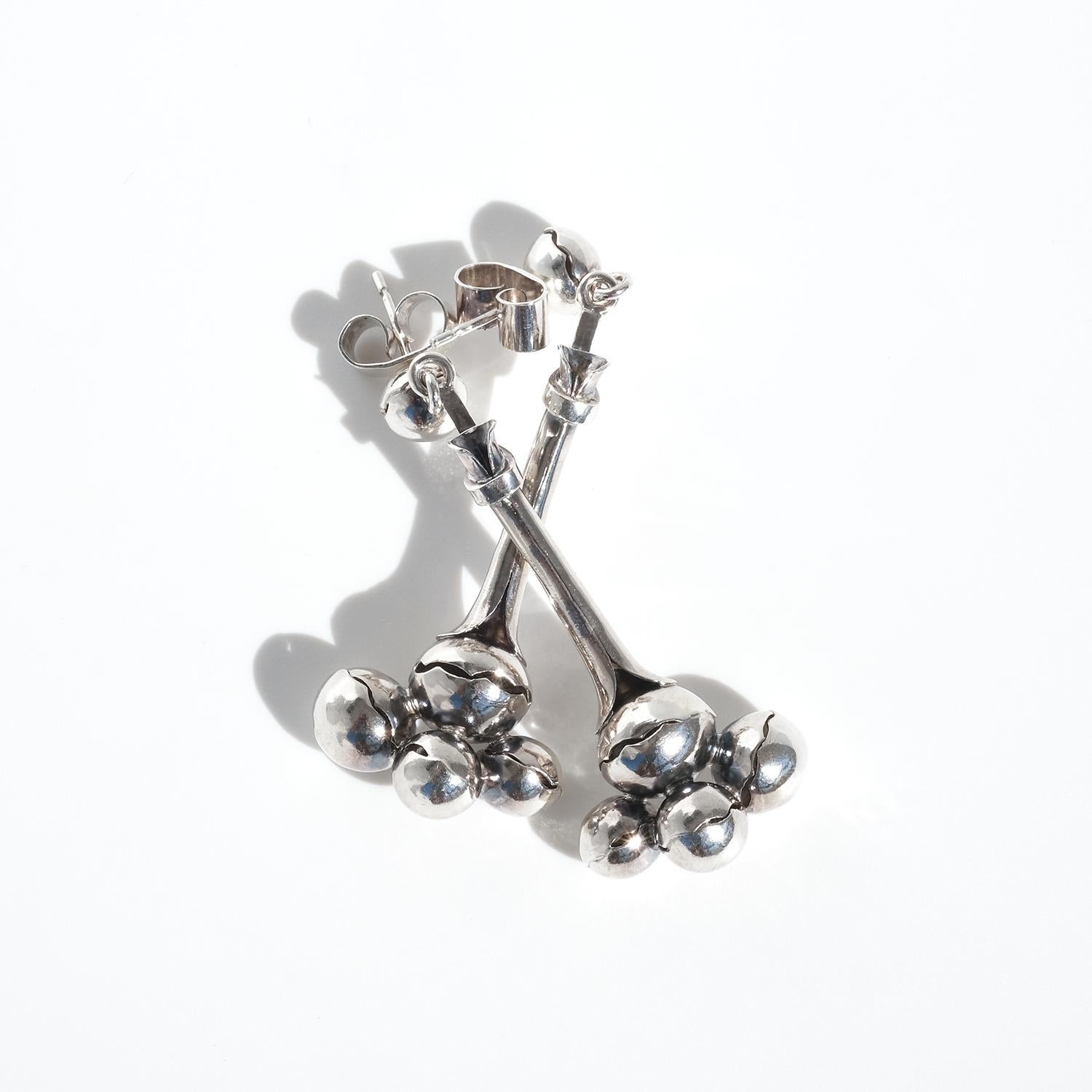 These vintage silver dangle earrings have a sculptural, organic design that feels both delicate and artistic. At the top, a smooth silver globe serves as a stud, securing the earrings comfortably against the ear. From this, a slender silver element
