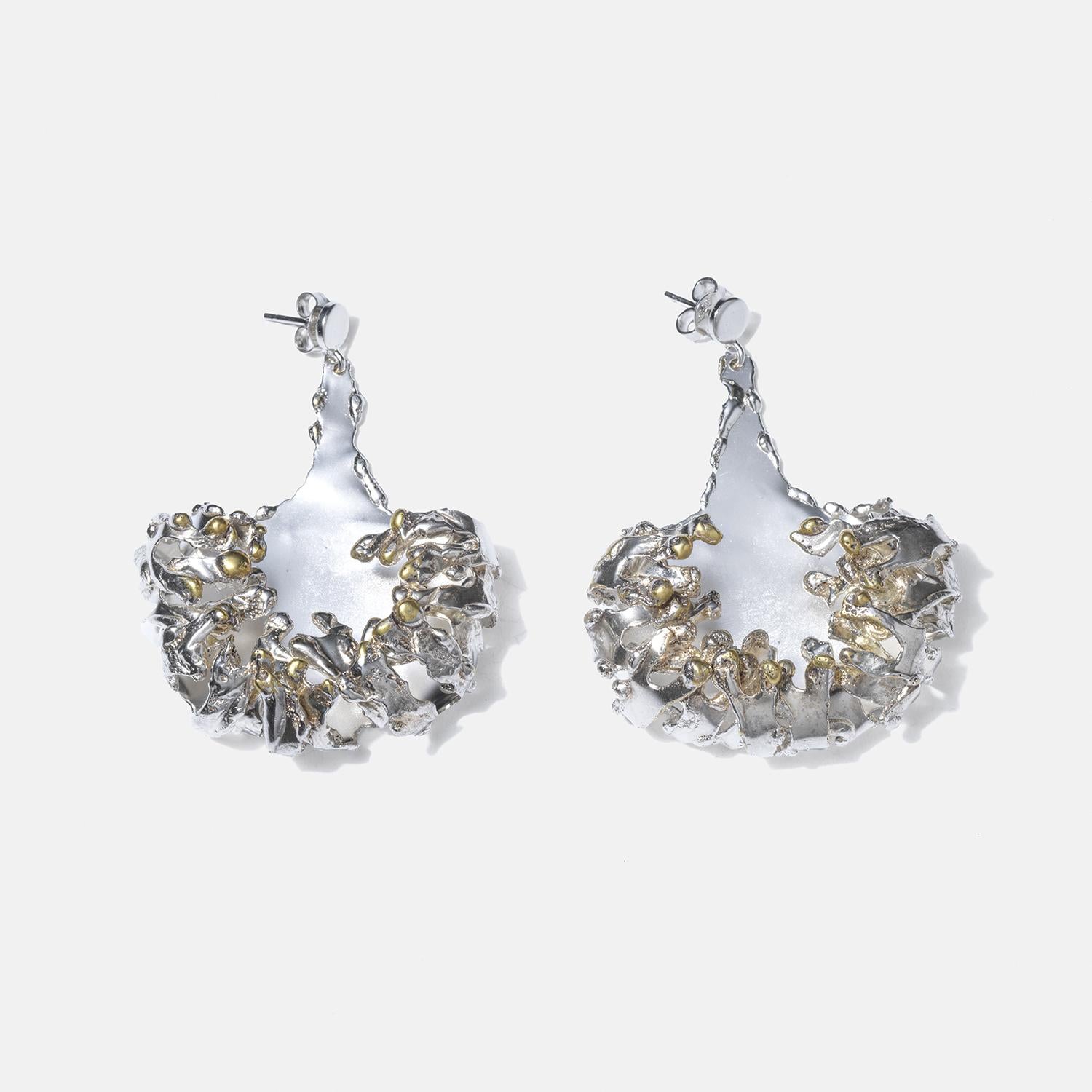 These striking silver dangling earrings feature an organic, molten-like shape, with fluid contours and a textured surface. The earrings are highlighted by gilded silver accents, which add a touch of contrasting warmth to the predominantly silver