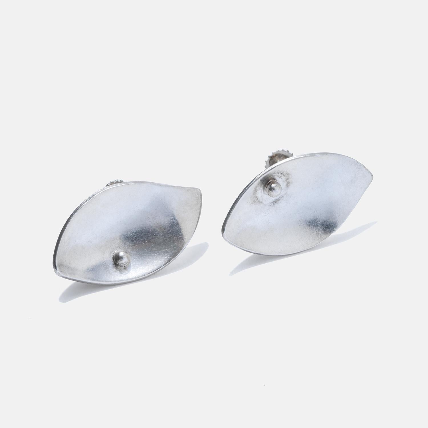 These sterling silver earrings have a sleek leaf-shaped design with a smooth, reflective surface. The earrings are designed to sit flush against the earlobe, creating an elegant and subtle look. Their simple yet stylish leaf shape gives them a