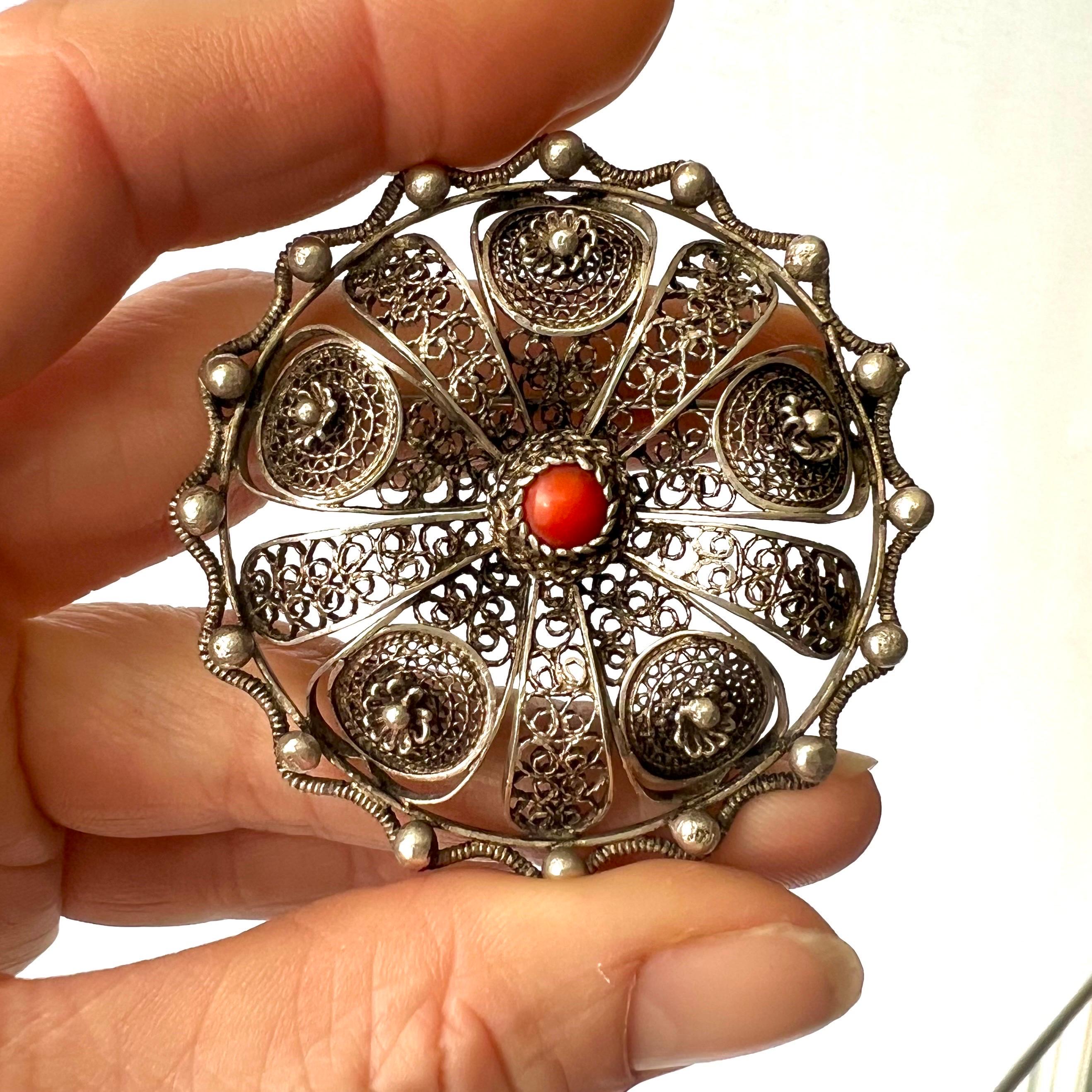 This is a lovely vintage silver round brooch created with fine rosettes and filigree work. The brooch is crafted with very fine filigree, floral rosettes and one coral stone in the center. The border is applied with small silver balls decorated with