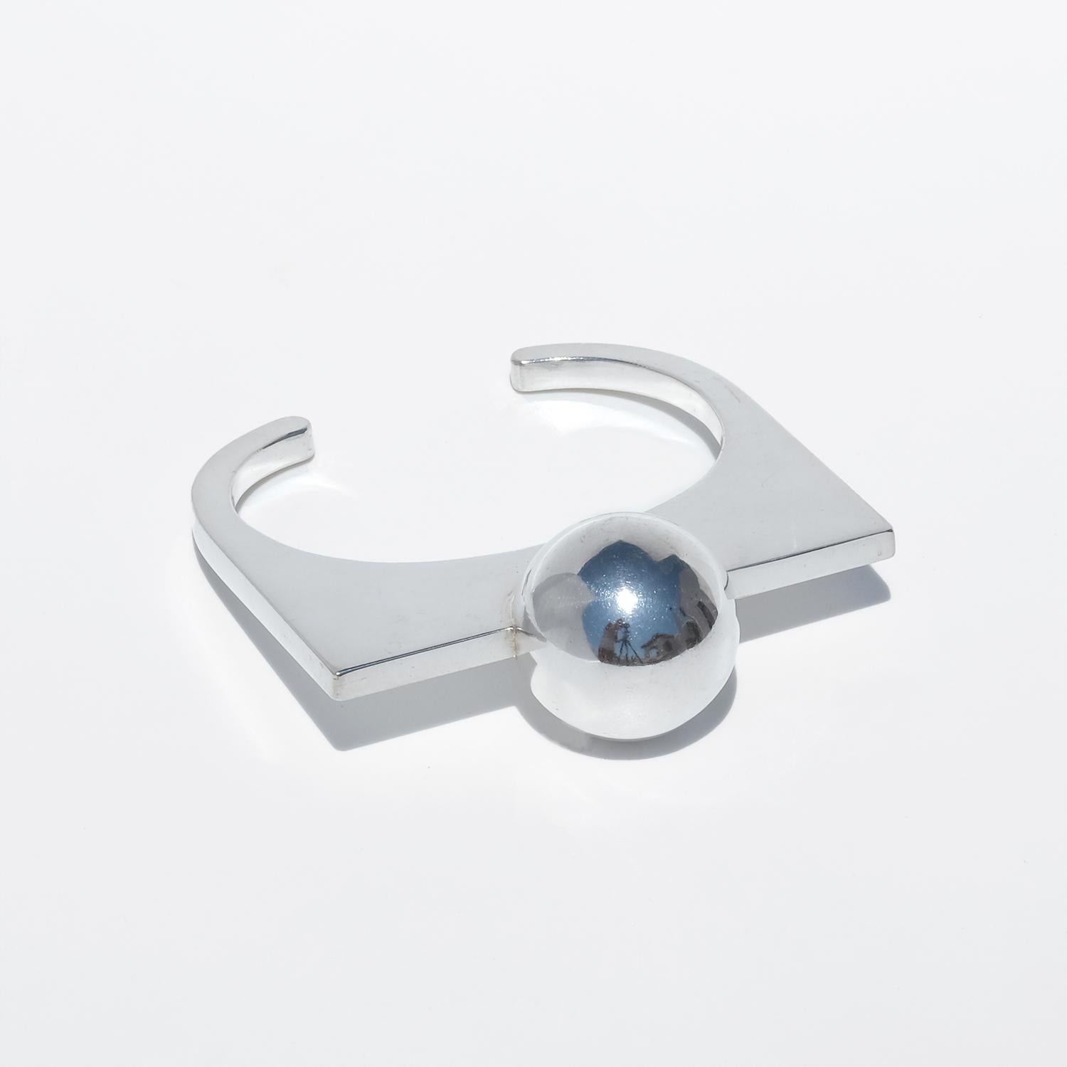 Il s'agit d'un bracelet manchette fixe en argent sterling poli. La bande est ouverte à l'arrière, formant un U fixe et non ajustable aux extrémités carrées. La partie supérieure est une large barre plate qui s'étend horizontalement sur le poignet,