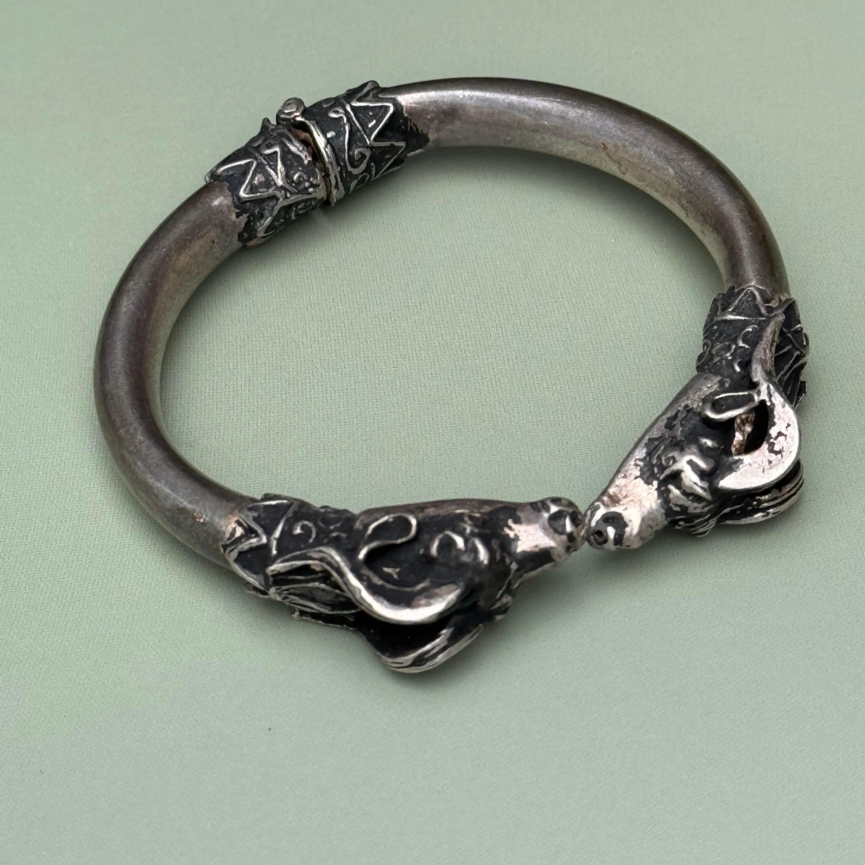 Bracelet features intricately detailed rams' heads, symbolizing strength and power, facing each other as if in a kiss. The hinged design allows for easy wearing and removal. The vintage aesthetic adds a touch of timeless elegance to any