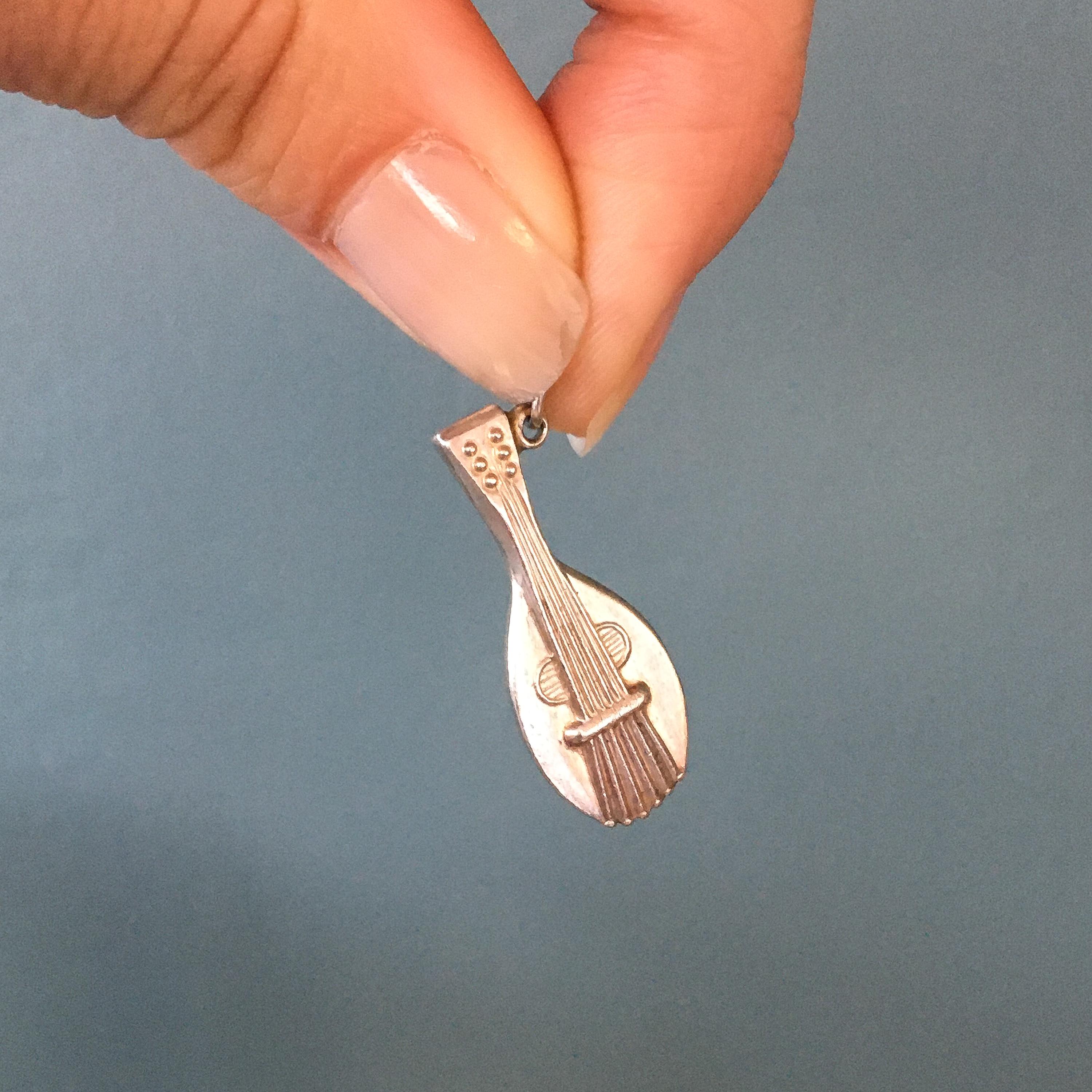Vintage silver mandolin guitar charm pendant. This detailed three-dimensional charm is made of silver. It's a lovely charm to add to your charm bracelet, wear as a necklace, or stacked with your favorite pieces.

The charm is in very good