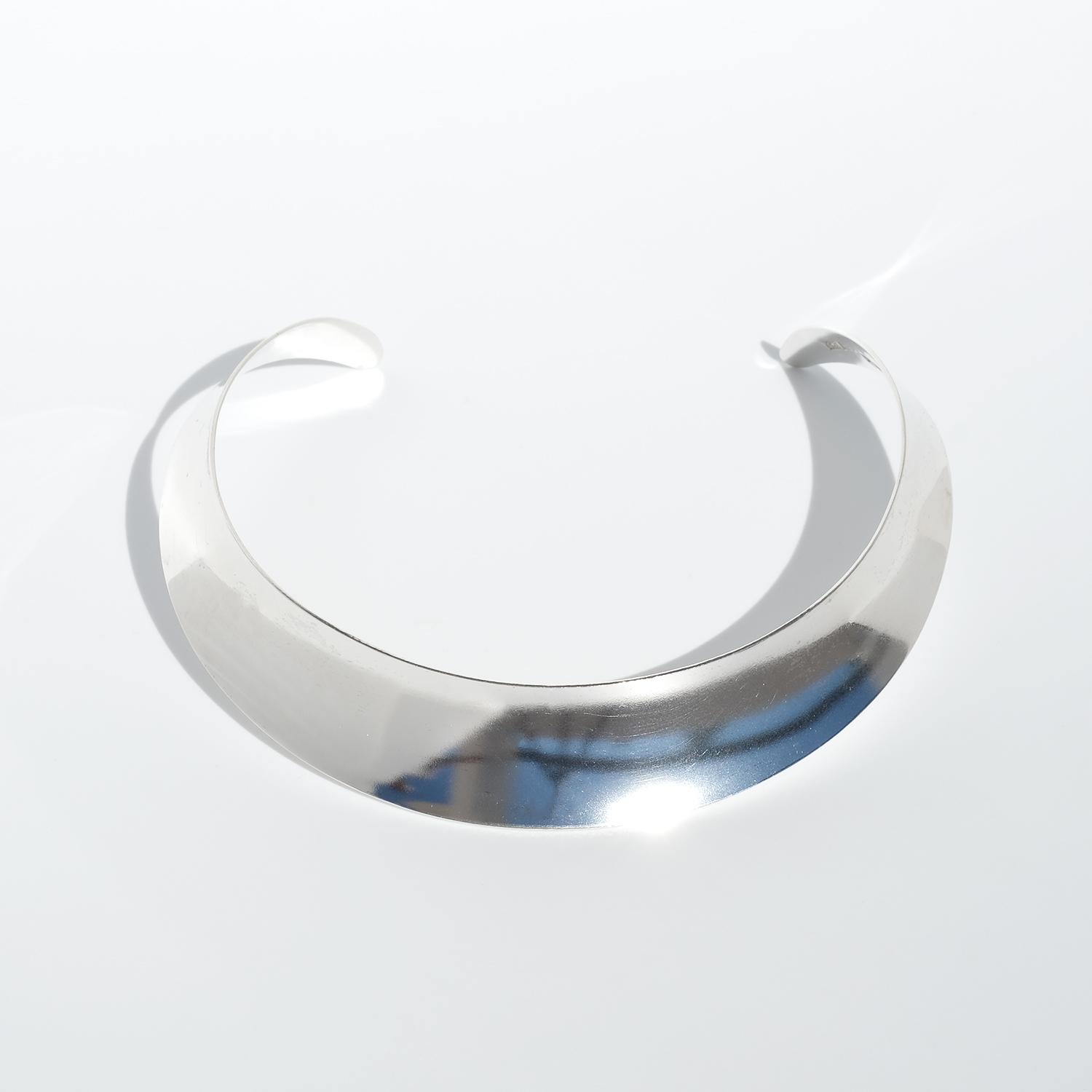 Questo anello da collo è meticolosamente realizzato in argento sterling e presenta un'ampia fascia fissa che si curva con eleganza per adattarsi comodamente al collo. La superficie dell'argento vanta una lucentezza brillante, che esalta la