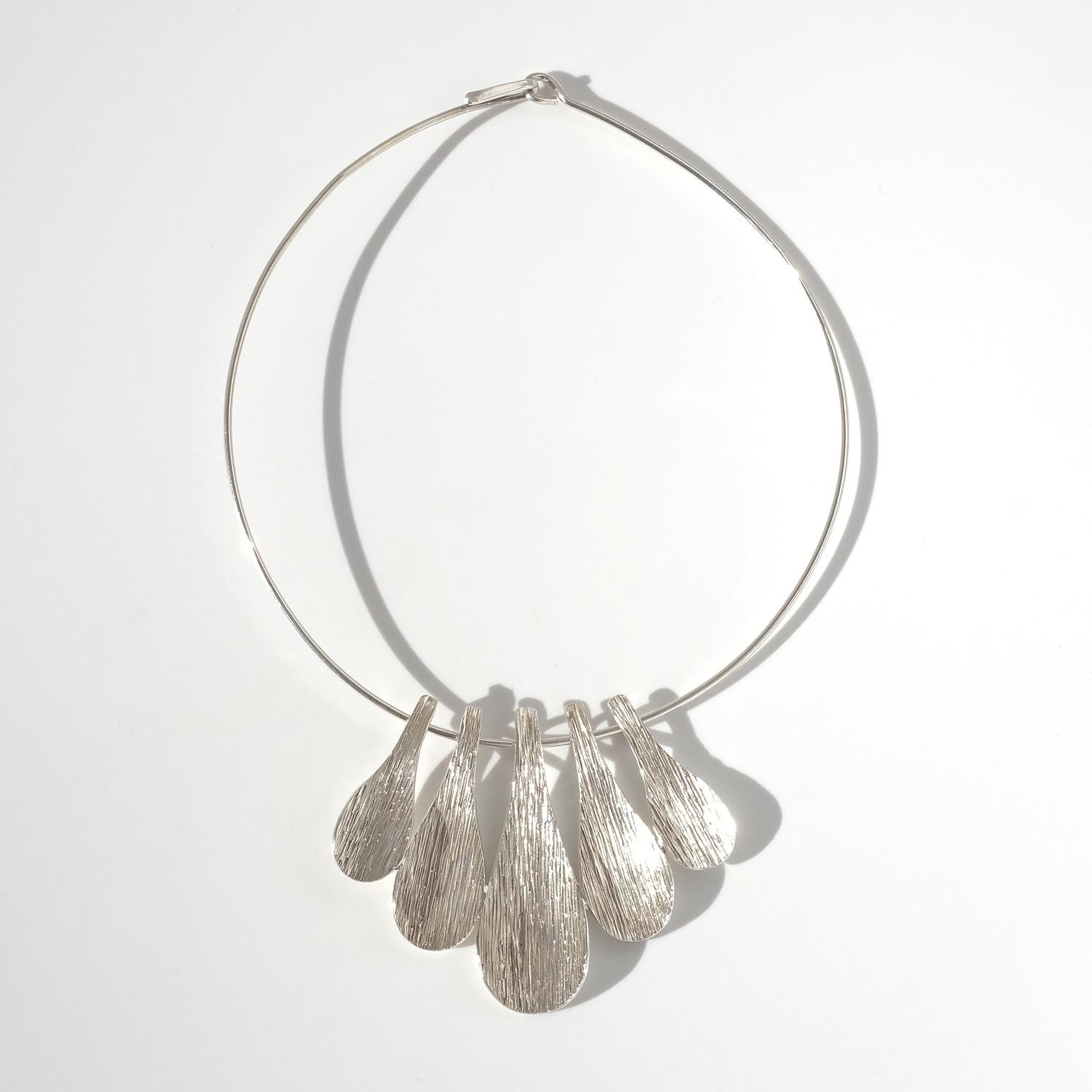Questo anello da collo vintage in argento è caratterizzato da un design elegante e minimalista che si adatta perfettamente al collo, creando un look audace e moderno. Il ciondolo è composto da cinque elementi allungati a forma di goccia di lunghezza