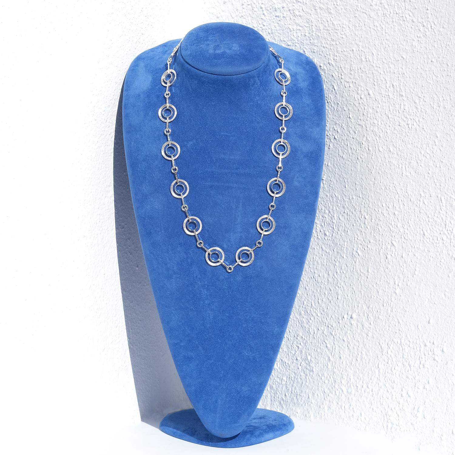 This vintage silver necklace features a series of interlinked double-ring motifs, creating a structured yet fluid design. Each element consists of a larger outer ring with a subtly etched, irregular texture, encircling a smaller, smooth inner ring.