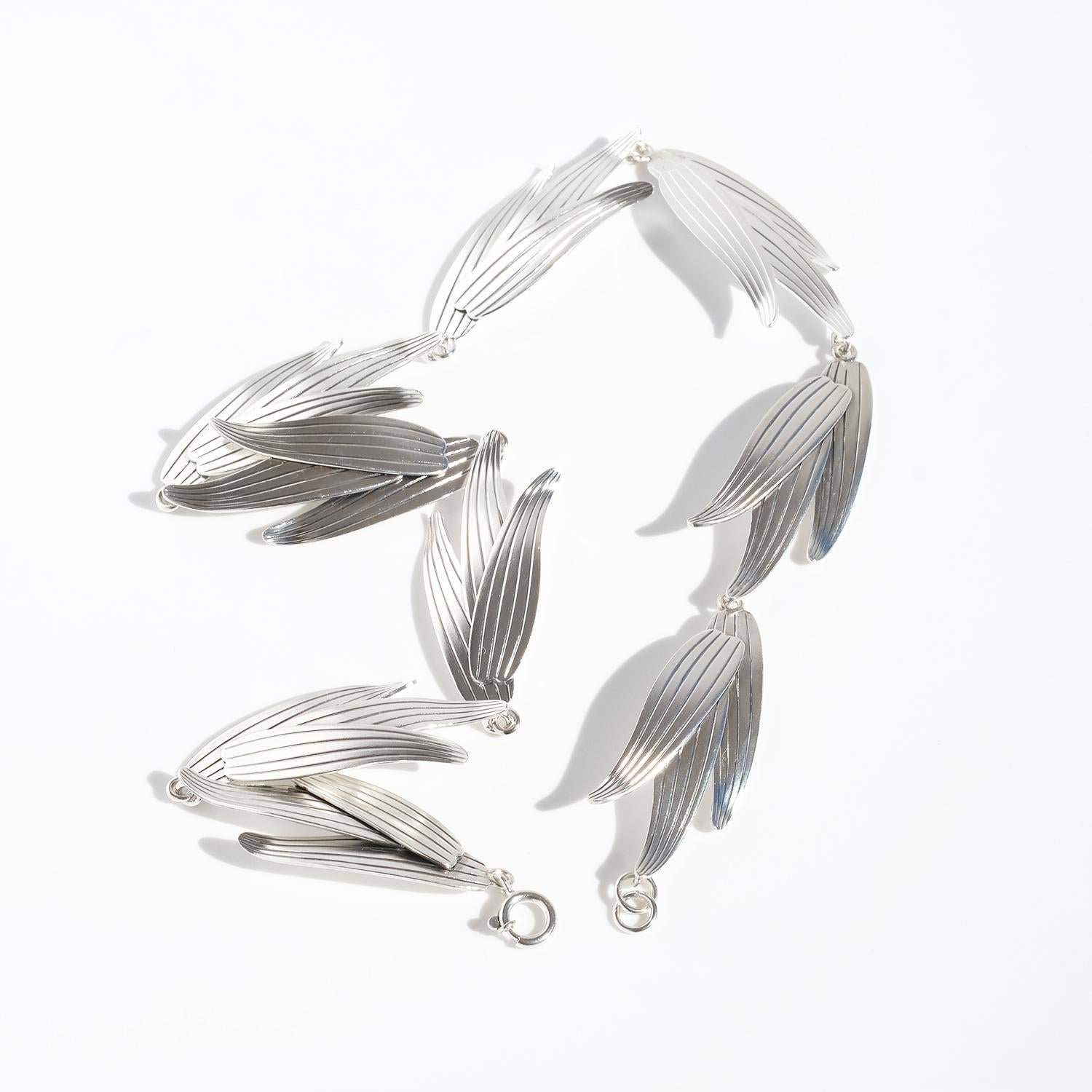 This vintage silver necklace features a series of elongated, leaf-like elements linked together in a flowing, organic design. Each piece is slightly curved, creating movement and dimension. The front of the leaves has fine, parallel engravings that