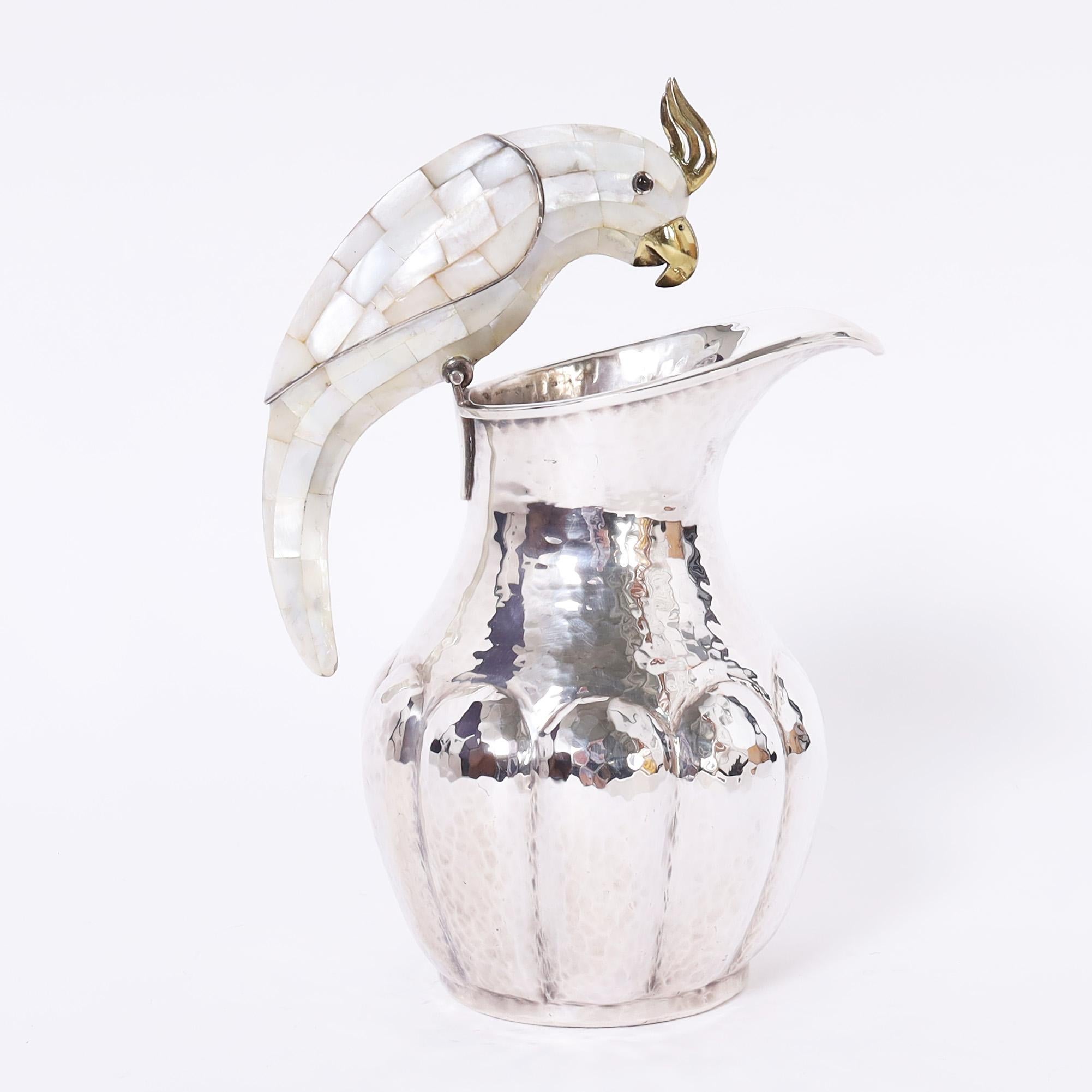 Striking mid century pitcher hand crafted in hammered copper with a silver plate finish featuring a bird clad in mother of pearl as a handle. Signed Mexico on the bottom. 