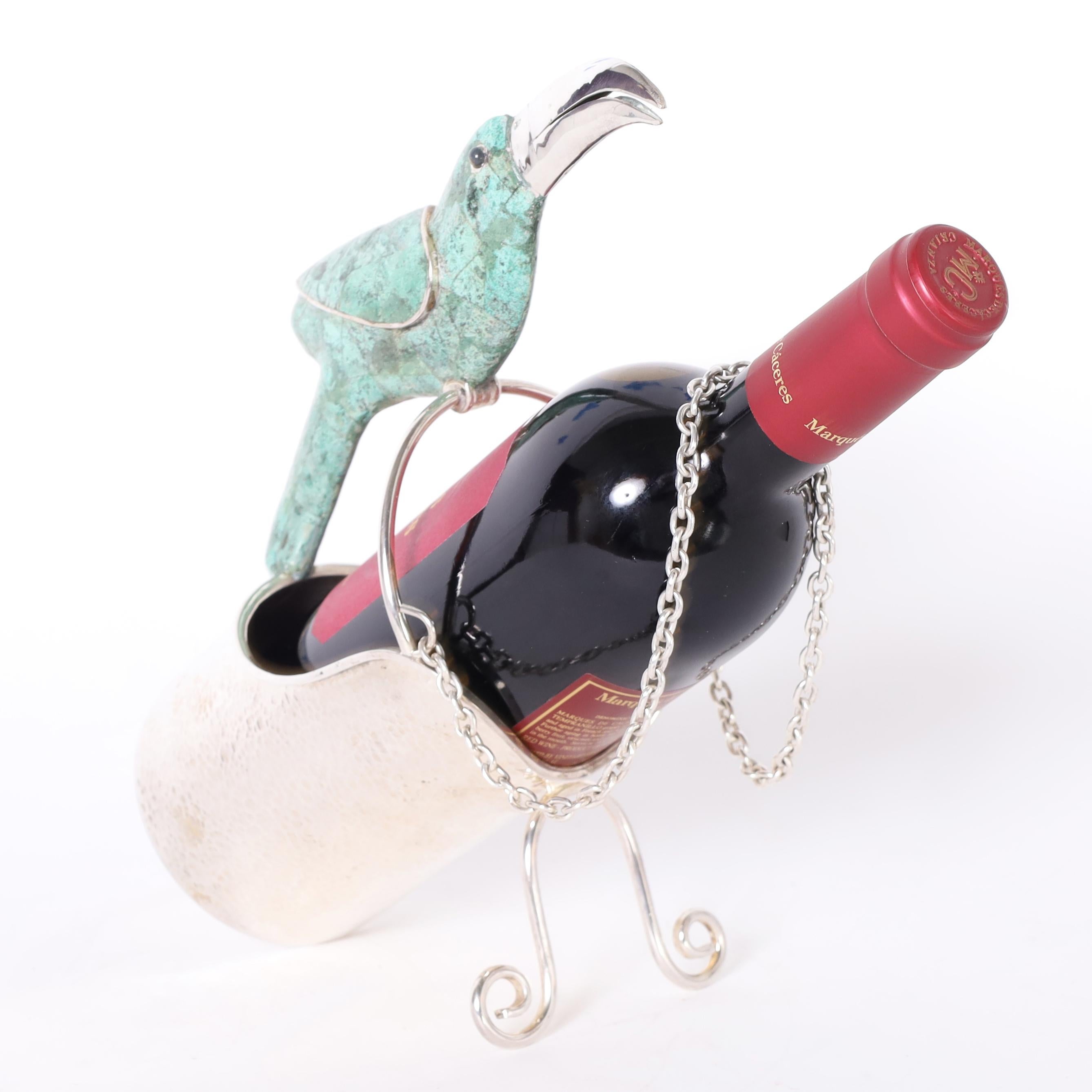 Refinado y caprichoso soporte para vino o botellas, hecho a mano en chapa de plata sobre cobre martillado, con un tucán revestido de piedra como asa. Estampado México en la parte inferior.