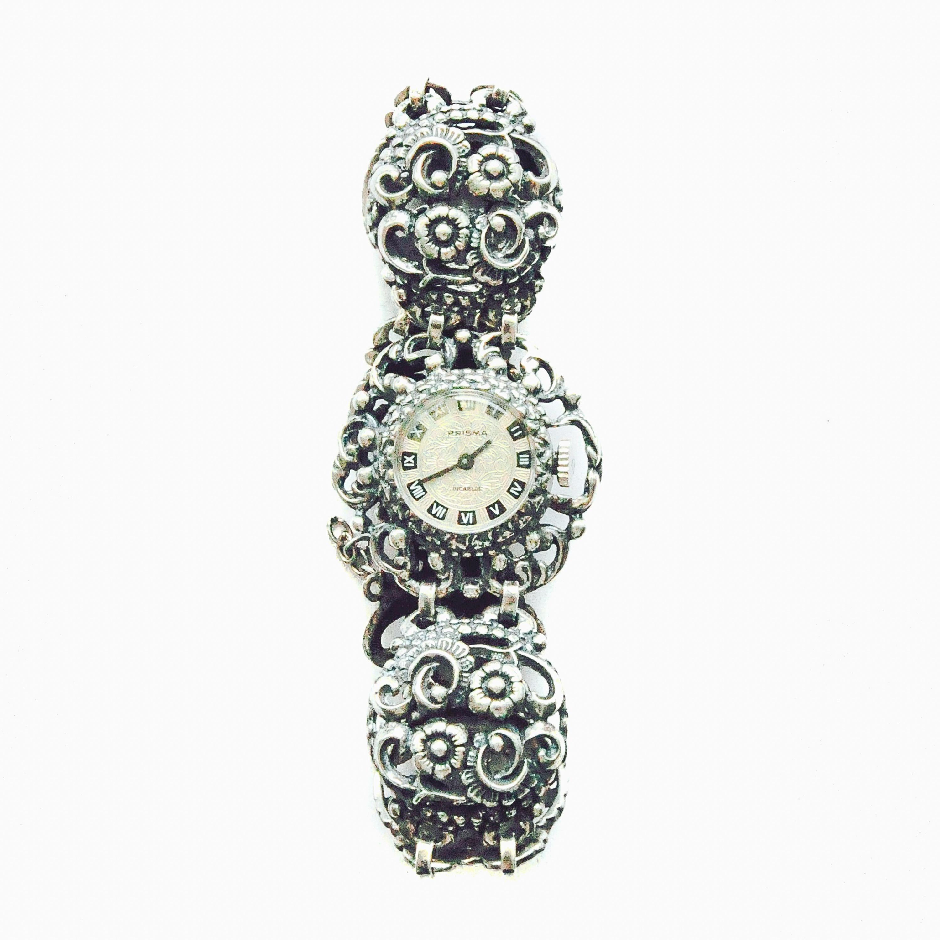A vintage silver 835 watch with a quartz movement. This open-worked bracelet watch has the brand name Prisma and the movement is by winding it up manual. The watch has a floral decor, is in very good condition and is runs well. The dial has white on