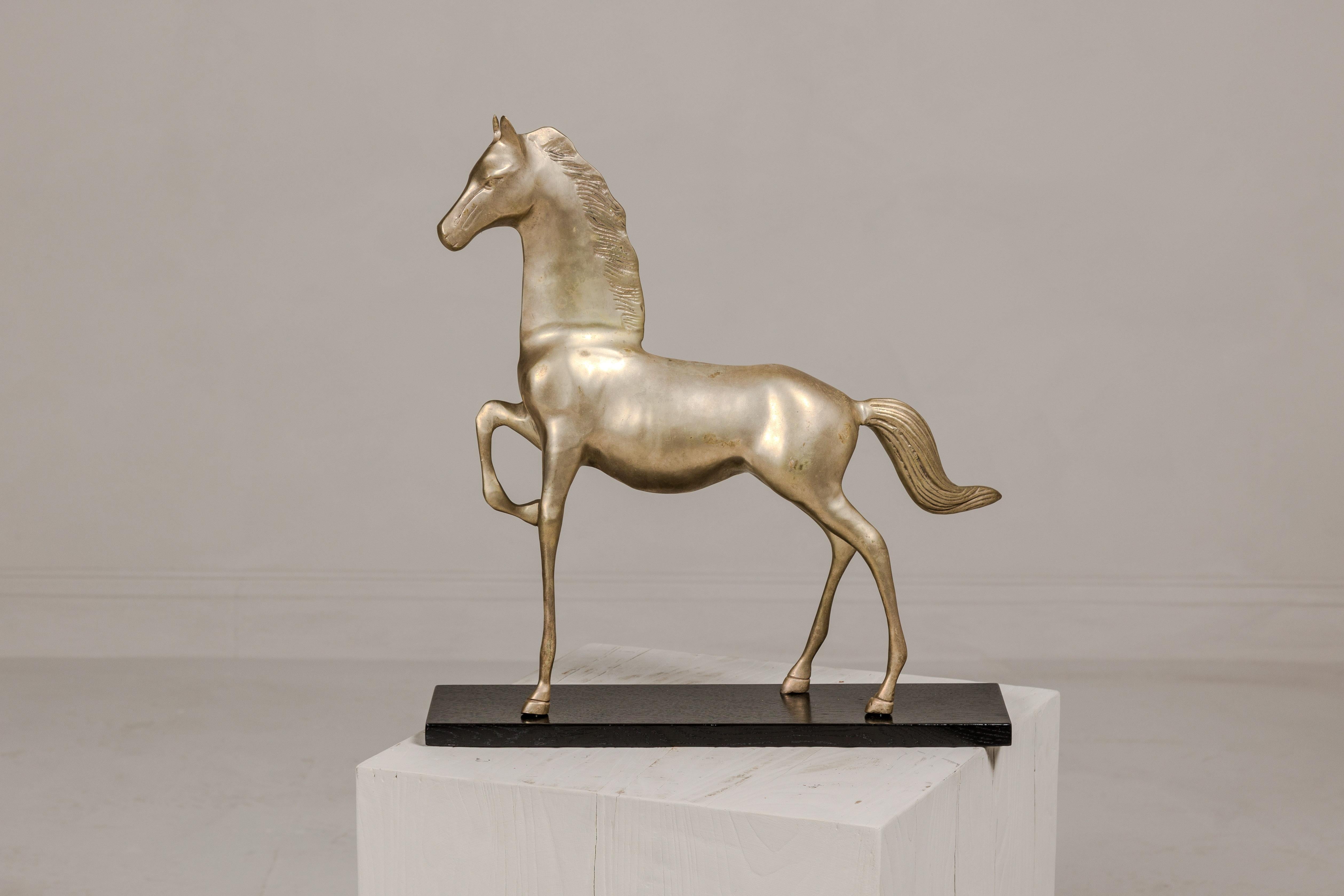 This vintage silver over brass walking horse statuette is an exquisite representation of equine grace and beauty, poised elegantly on an ebonized oak base. The statuette captures the majestic stride of the horse, with its right front leg raised in a