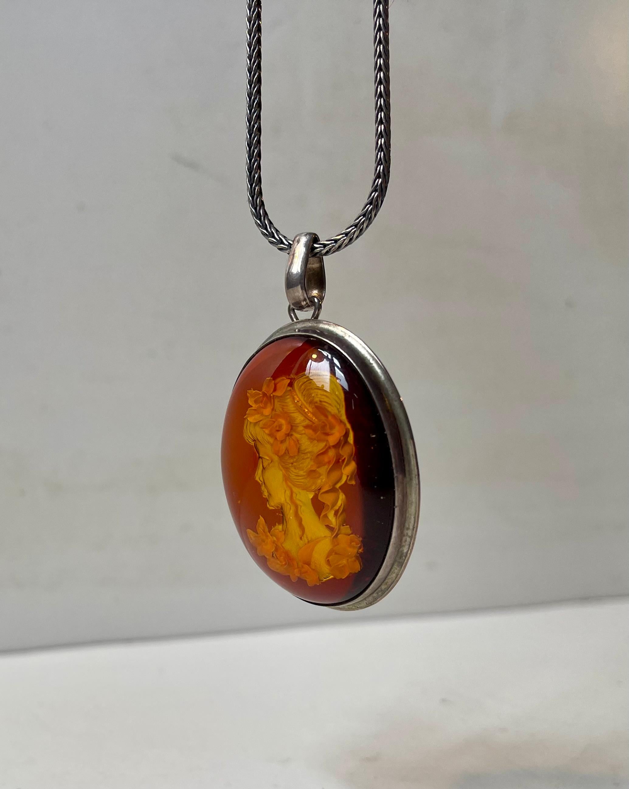 A set consisting of a long pleaded sterling silver necklace with a length of 60 cm and a hand-crafted cameo pendant finished in Baltic honey amber in reverse. Signed and hallmarked indistinguishable by the maker. The pendant measures: 50x40x1.3 mm