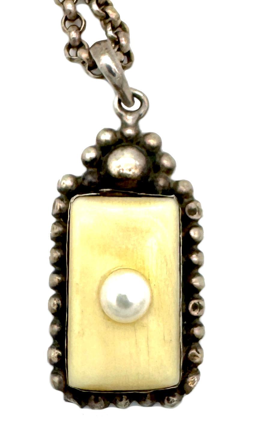 Questo ciondolo vintage è stato creato nell'ultimo quarto del XX secolo in argento. Un rettangolo in osso è incastonato in una montatura d'argento e decorato con una perla bouton bianca. Il ciondolo è accompagnato da una lunga catena d'argento.