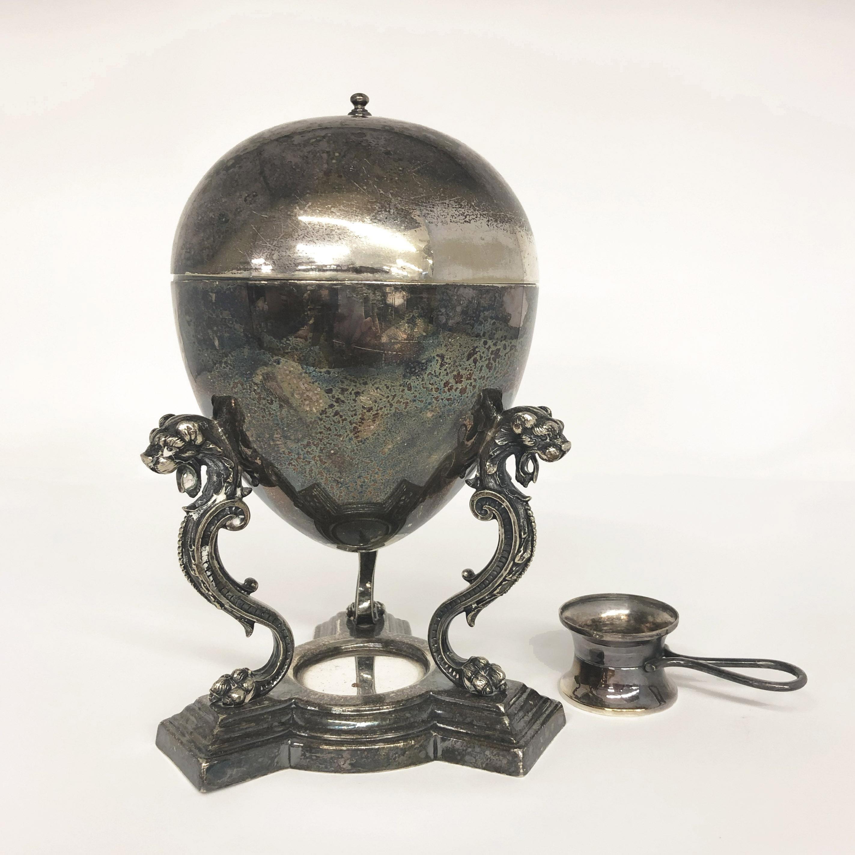 Vintage egg warmer, circa 1920, in silver plate, featuring three dragons on scrolled legs of the warmer base. Once a desirable table piece for elegant dining, eggs could be warmed at the table and served hot and fresh to diners. A burner sits