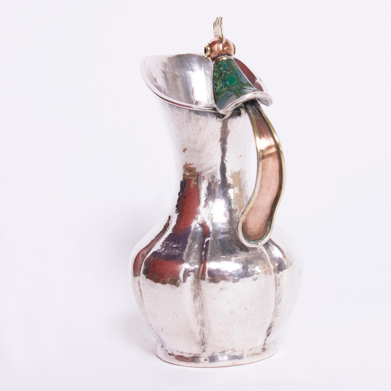 Standout Mid Century pitcher handcrafted in silver plate over hammered copper in classic modern form featuring a mixed metal stone clad bird as a handle. Stamped Los Castillo Mexico on the bottom.
